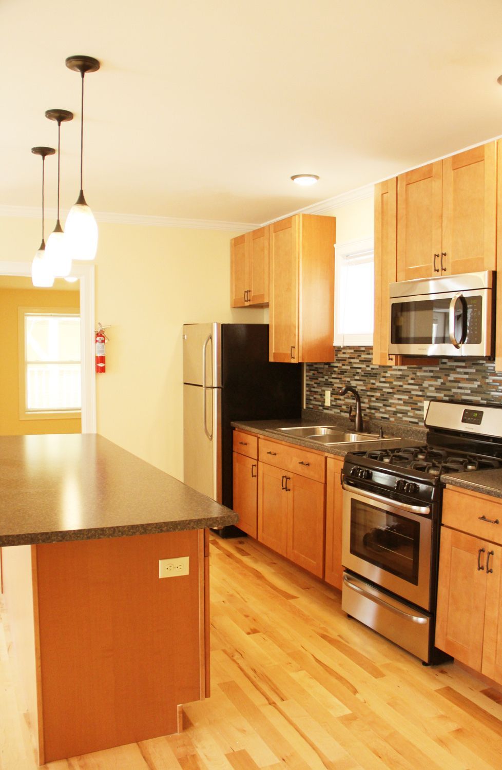 Kitchen with light wood cabinets, stainless steel appliances, and island with pendant lights.