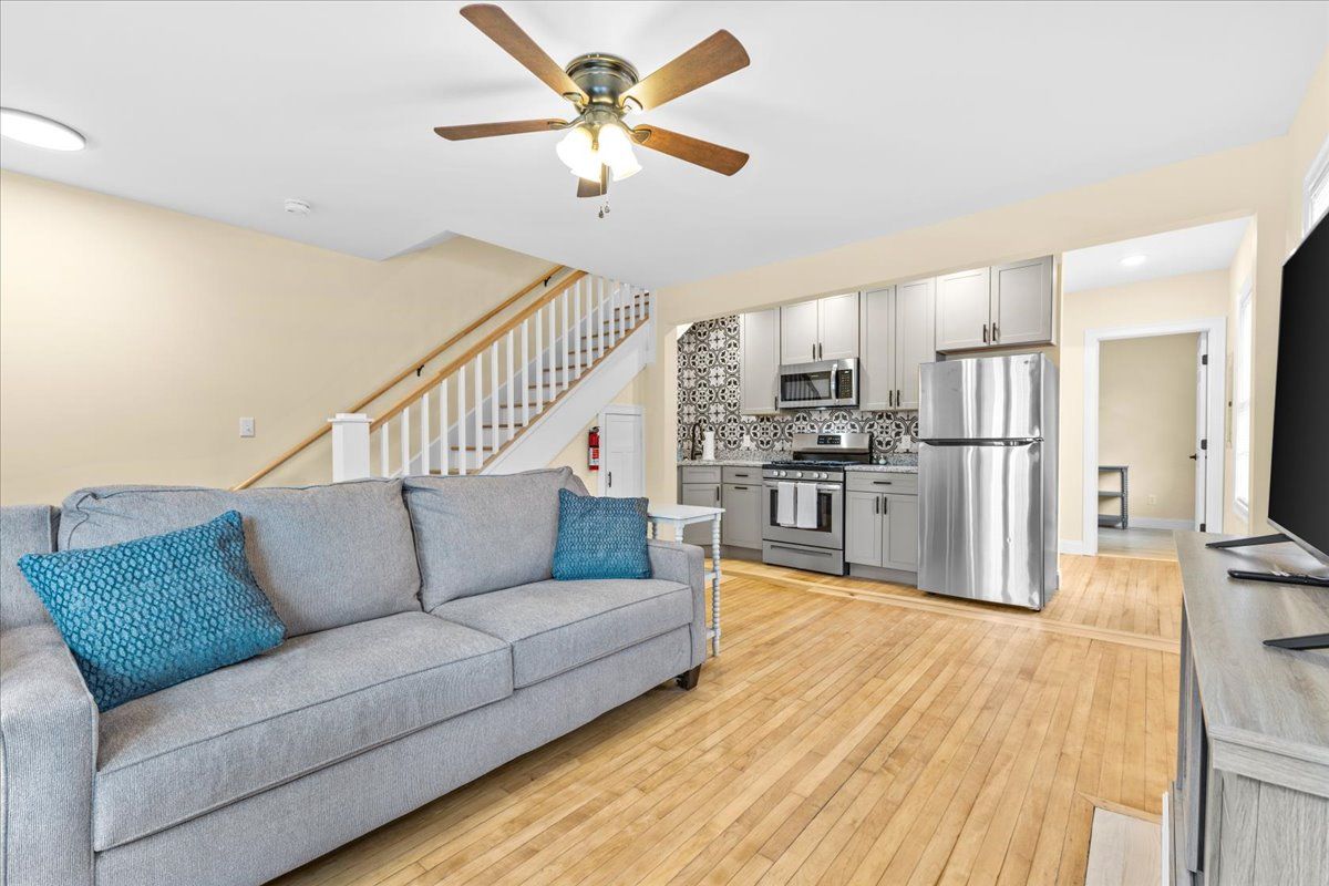 Living room with gray sofa, kitchen, stairs, and hardwood floors.