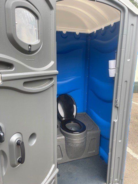 Gray and blue portable toilet, with open door revealing the toilet seat and roll holder.