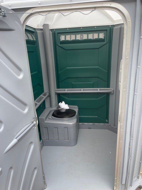 Interior of a portable toilet with green and gray plastic walls, a toilet, and a floor. Door open.