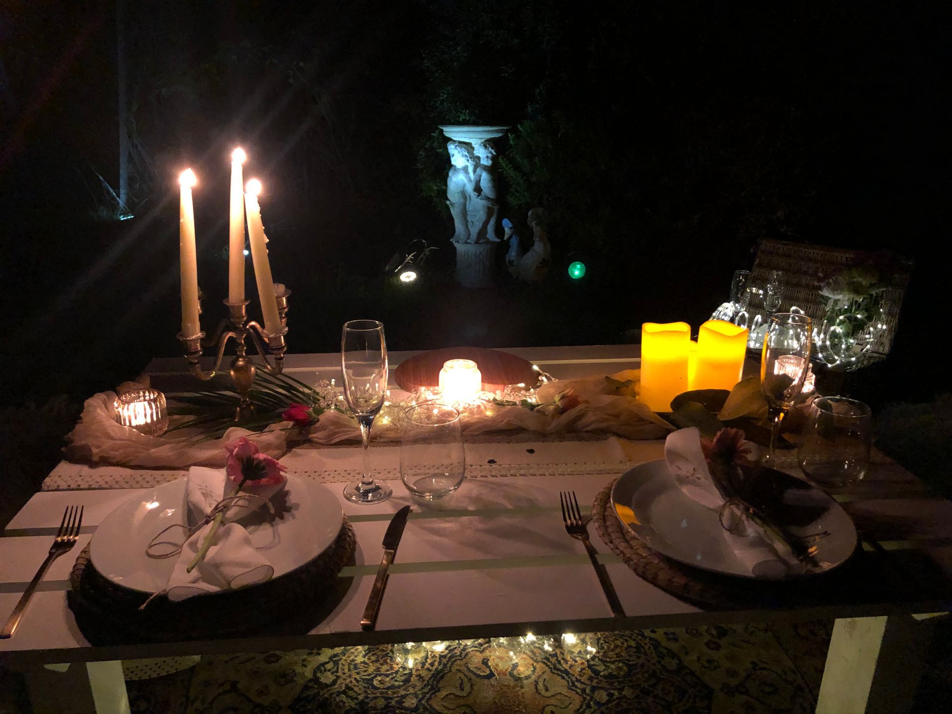 Romantic outdoor dinner setting with candles and statue.