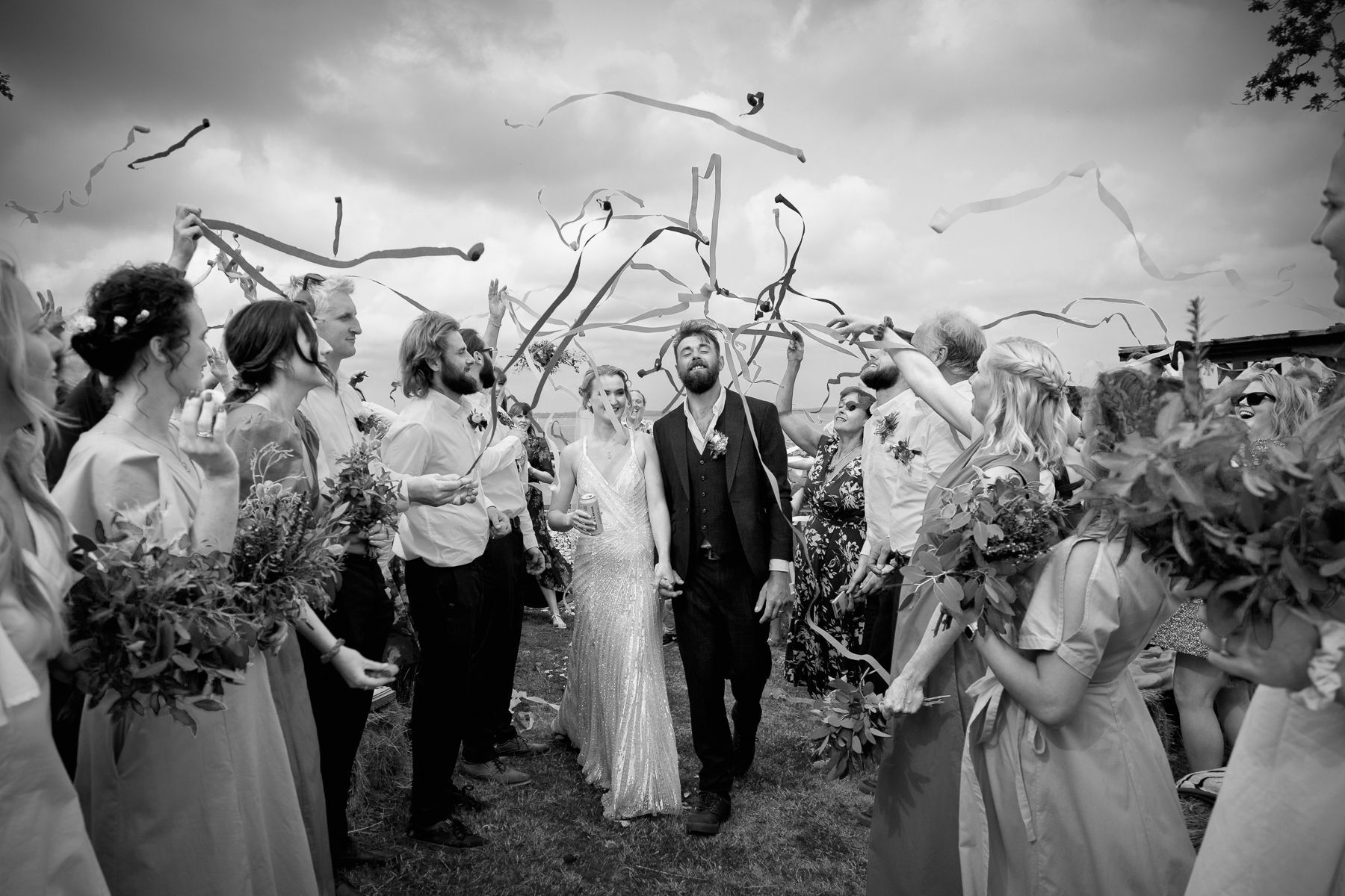 Newlyweds walk through guests, showered with streamers, on a cloudy day.
