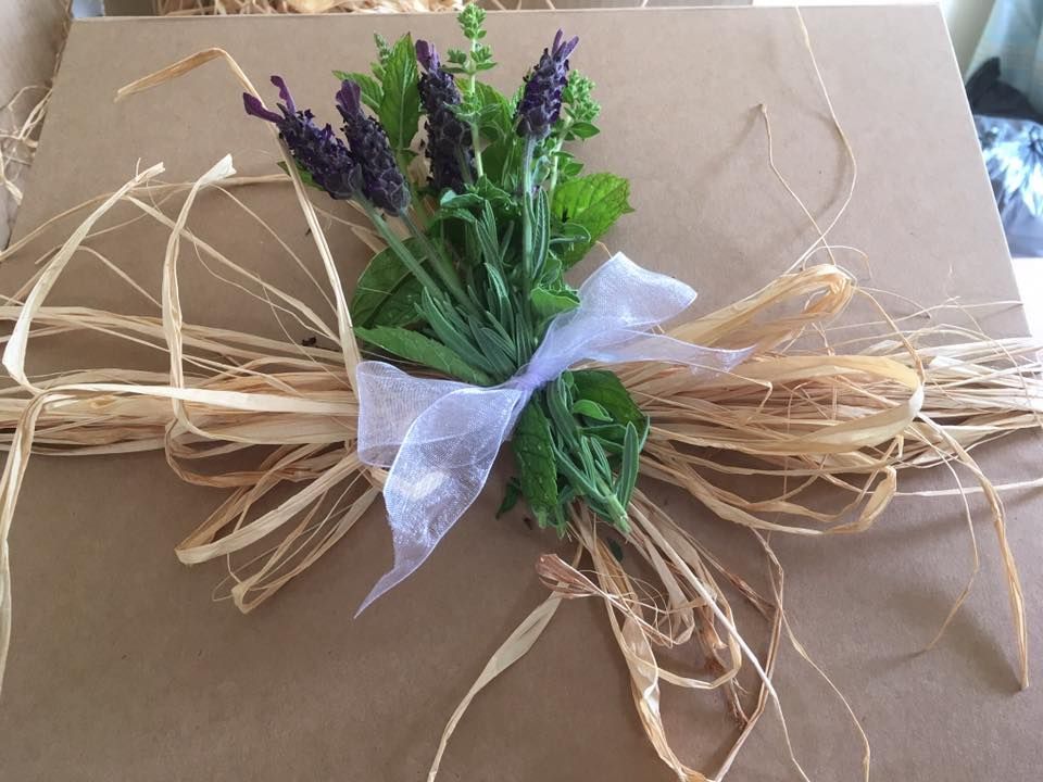 Brown gift box with lavender, greenery, white ribbon, and raffia.
