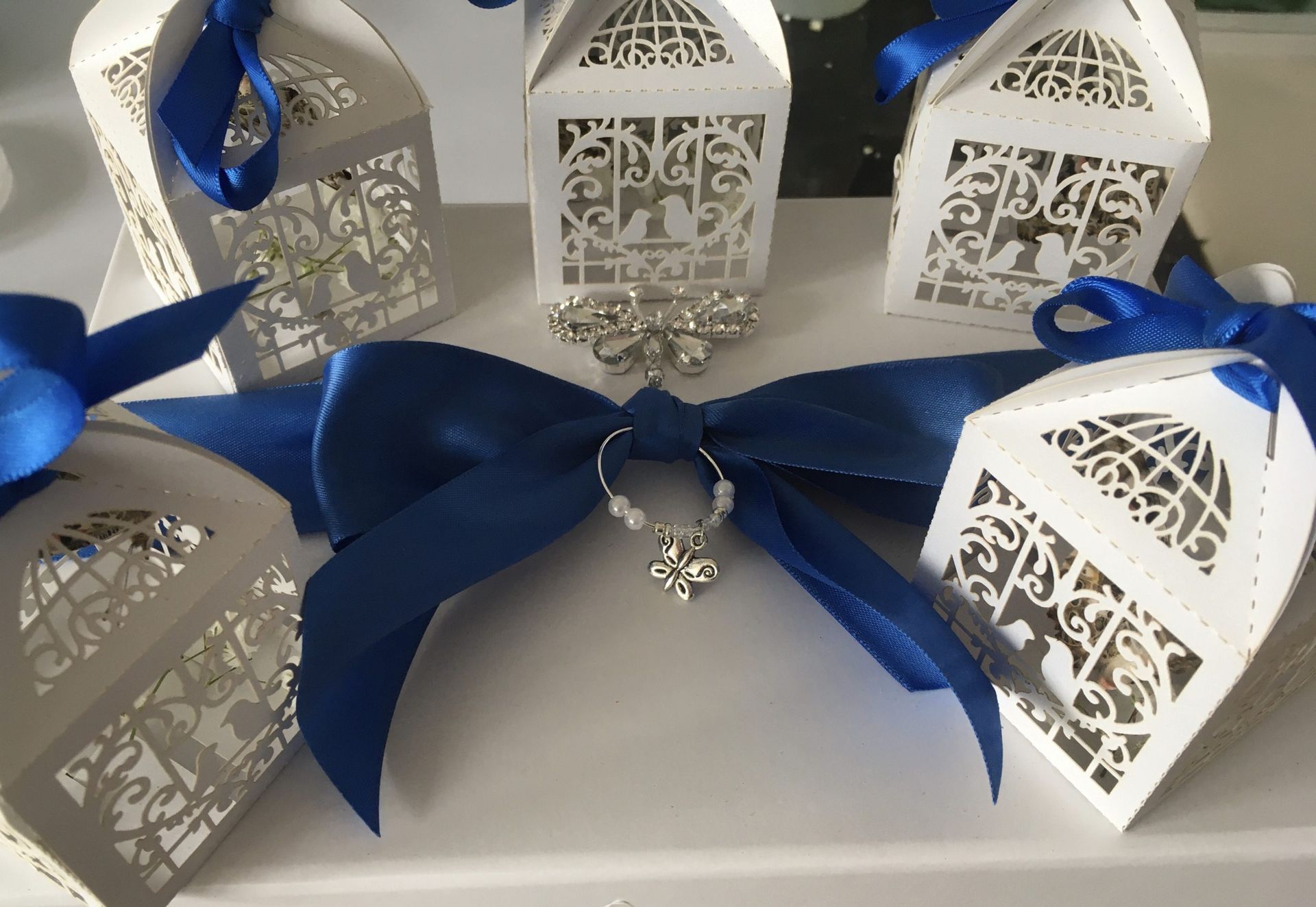 White laser-cut favor boxes with blue ribbon bows, set on a white surface.