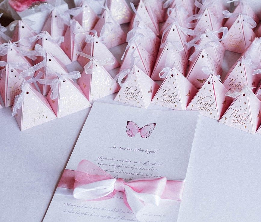 Pink pyramid-shaped gift boxes and a card with a butterfly illustration and ribbon on a white surface.