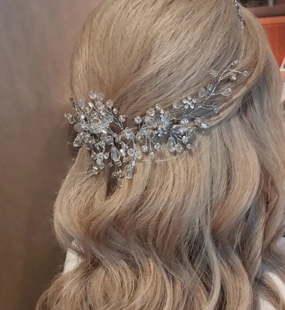Blonde hair with a silver crystal hairpiece, styled in waves.