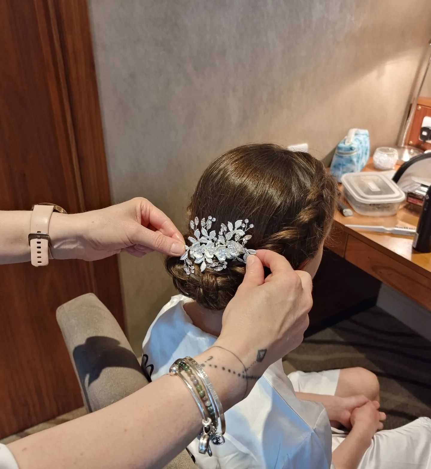 Person having hair styled, with a stylist adding a jeweled hair accessory. Indoors, neutral colors.