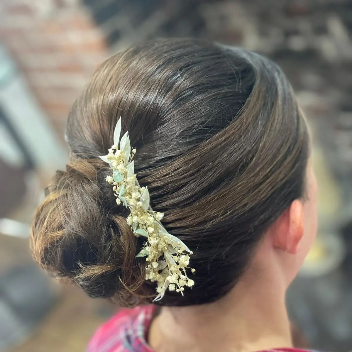 Woman's brown hair styled in a low bun, decorated with a floral hairpiece.