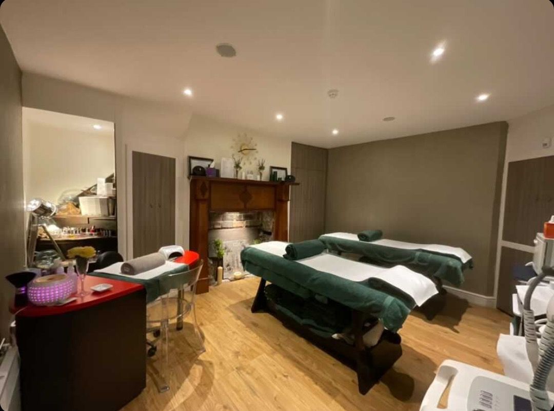 Two massage tables in a dimly lit spa room with fireplace, doorway, and medical equipment.