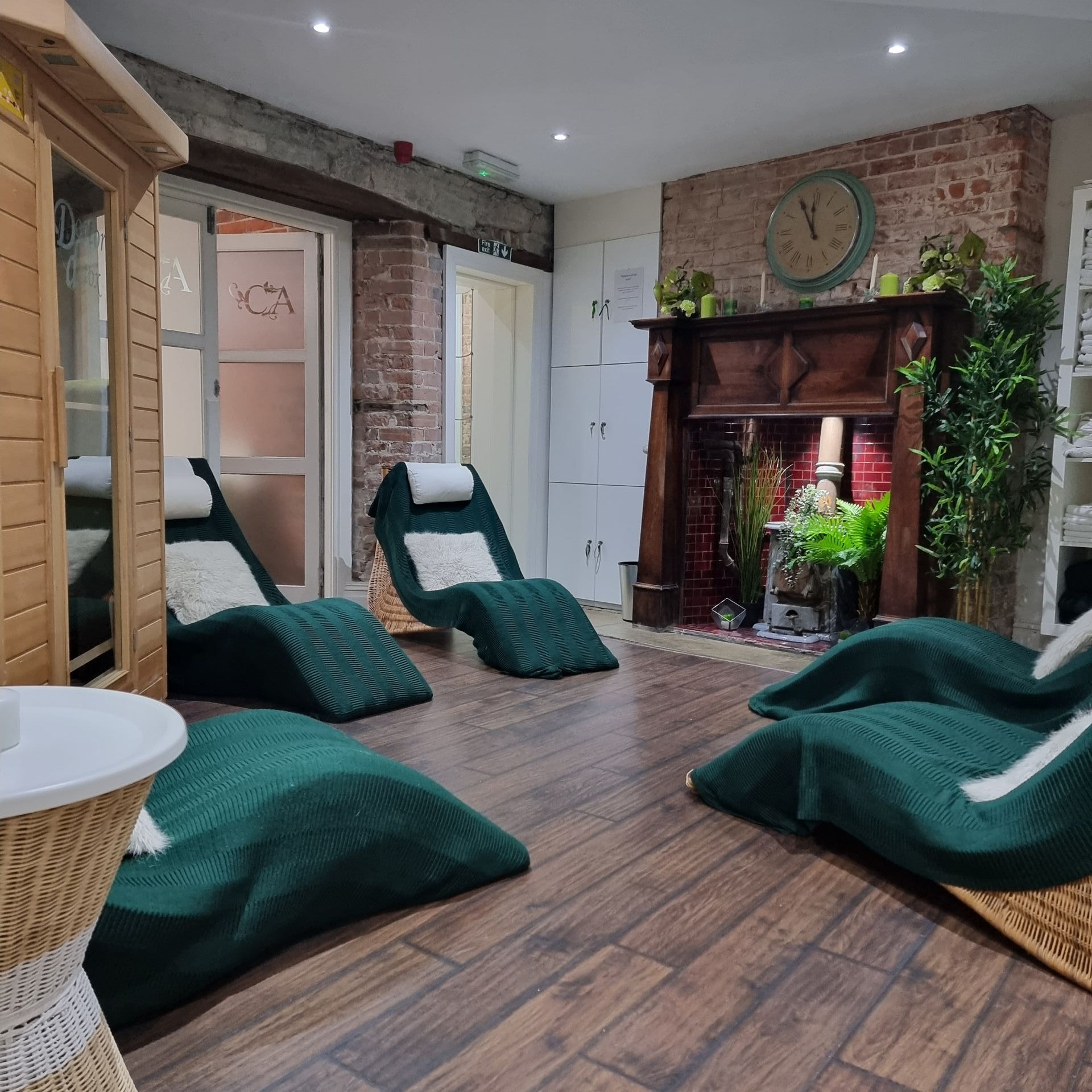 Relaxation room with green loungers, fireplace, wood floors, and small sauna.