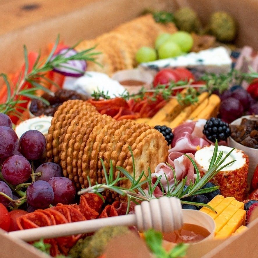 Charcuterie board with crackers, grapes, cheese, meat, and honey dipper.