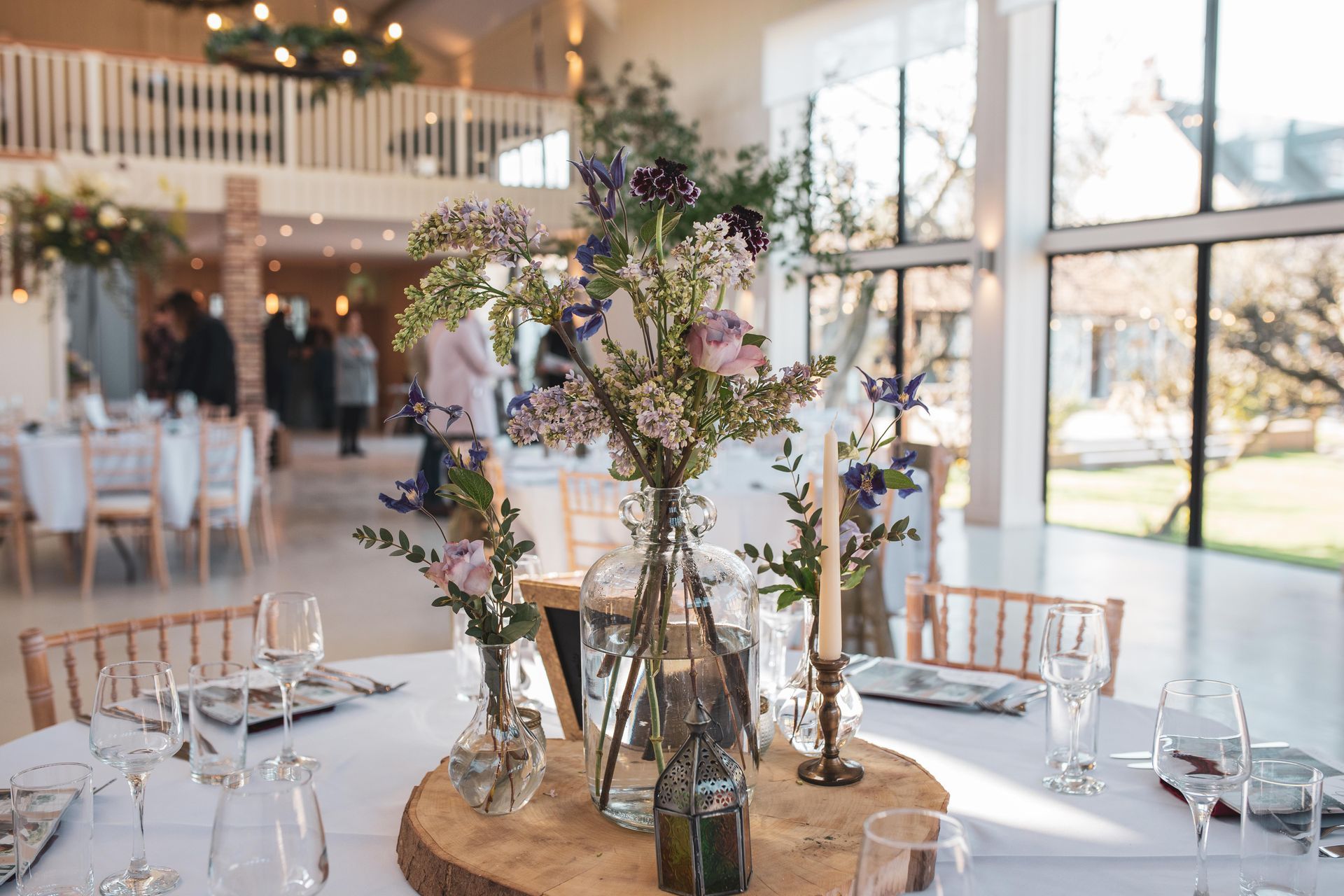 Wedding reception table setting with floral centerpieces, in a light-filled venue.