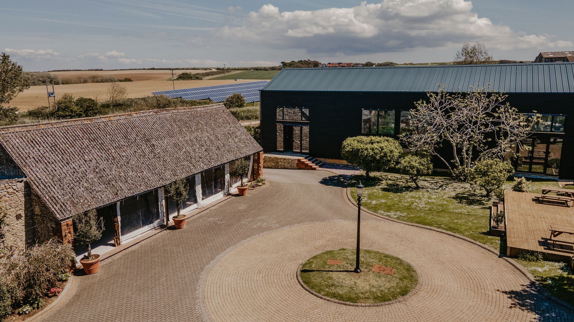 Buildings with black and brown exteriors, circular brick driveway, and rural landscape.