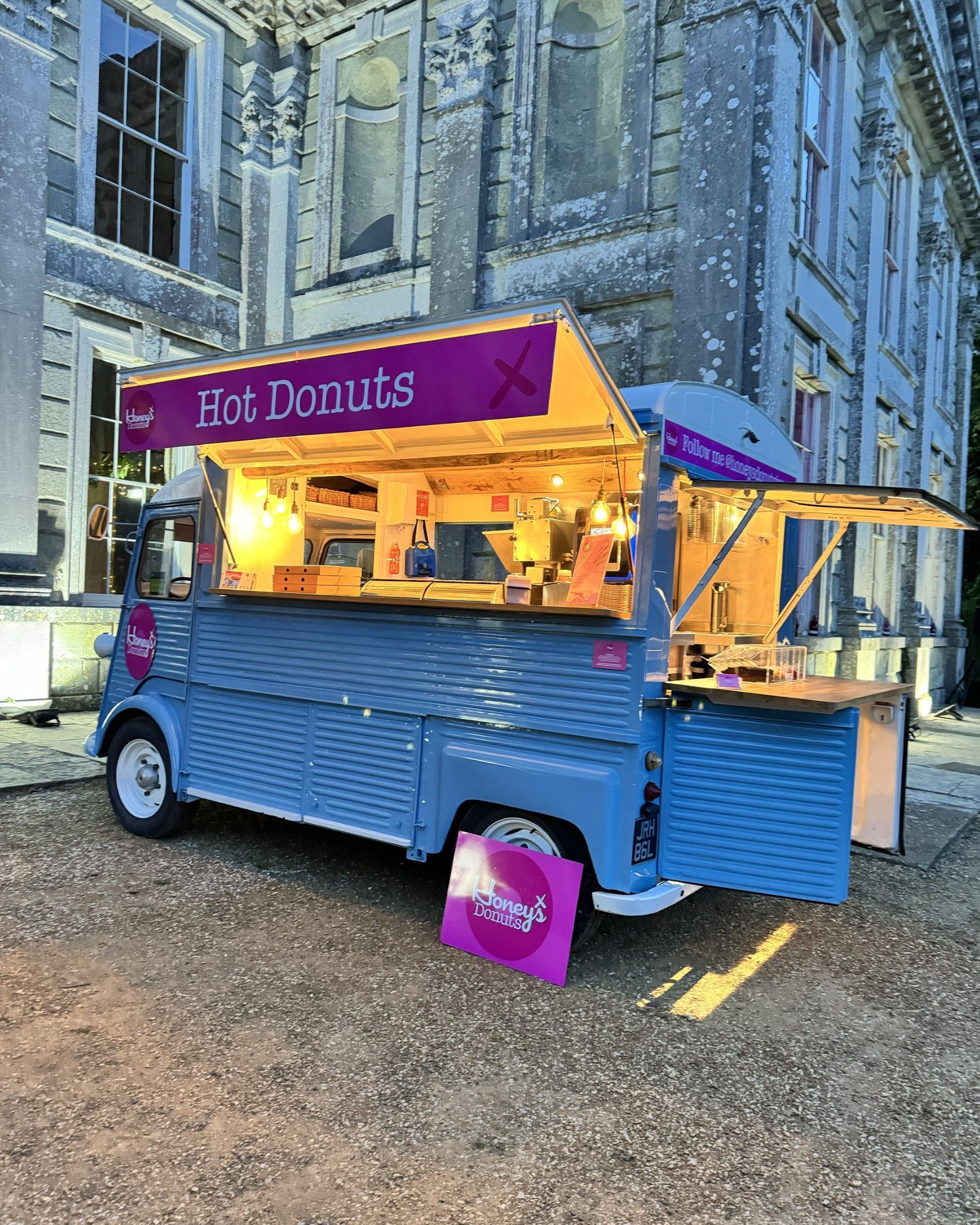 Blue donut food truck with pink signage set up in front of a large building.