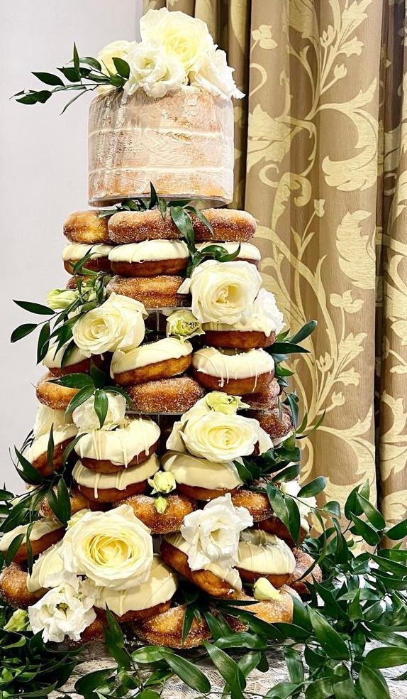 Wedding cake made of donuts and a small cake, decorated with white flowers and greenery.