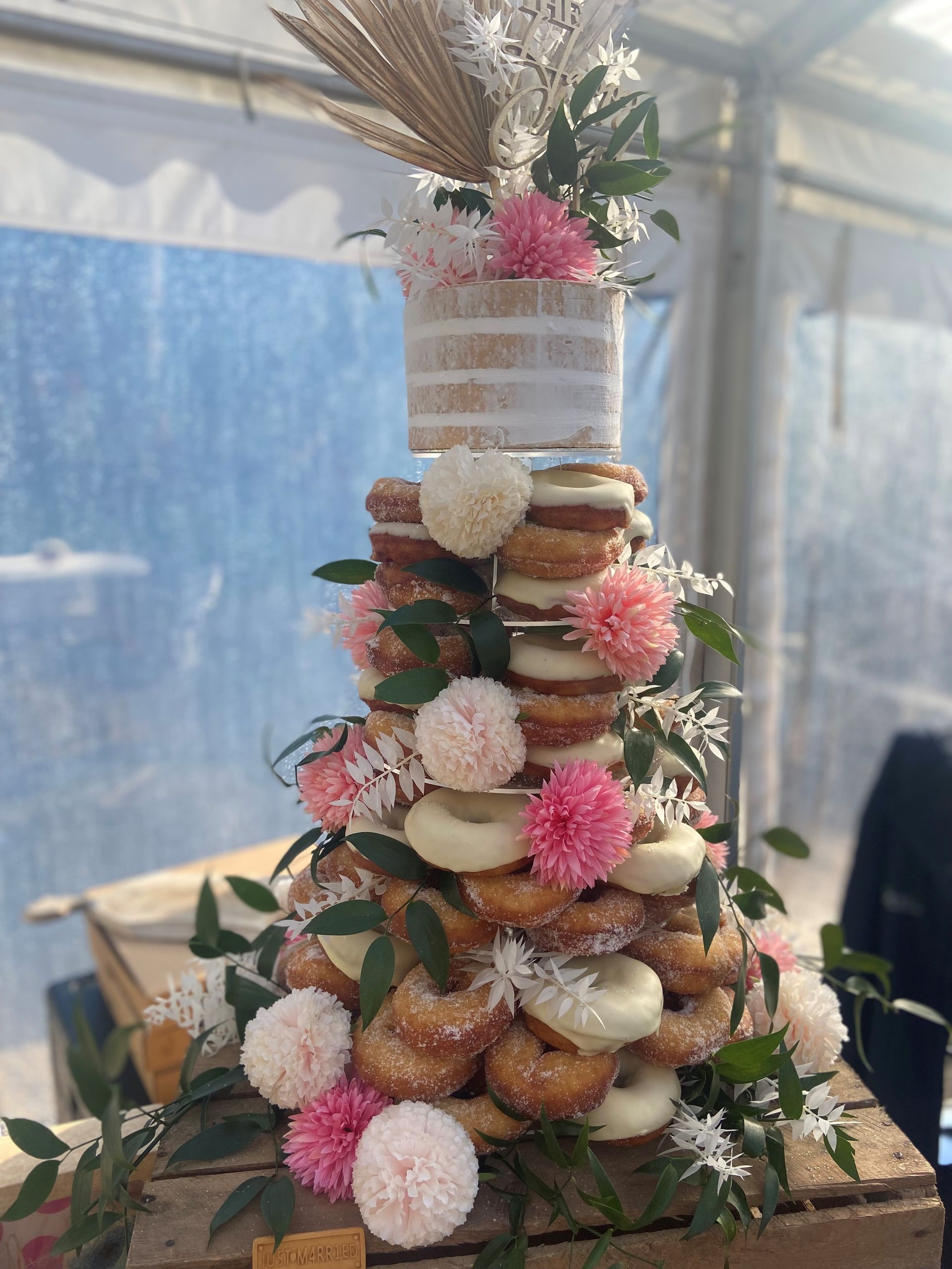 Wedding dessert tower: stacked donuts and cake, decorated with flowers and greenery.