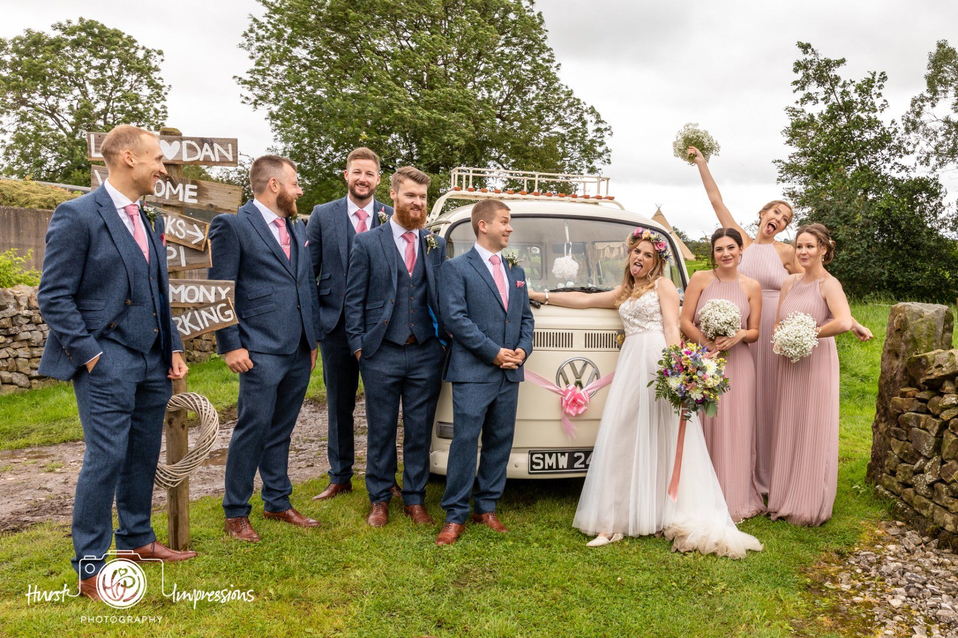 Wedding party poses by a vintage van; groom and groomsmen in navy suits with pink ties; bridesmaids in pink dresses.