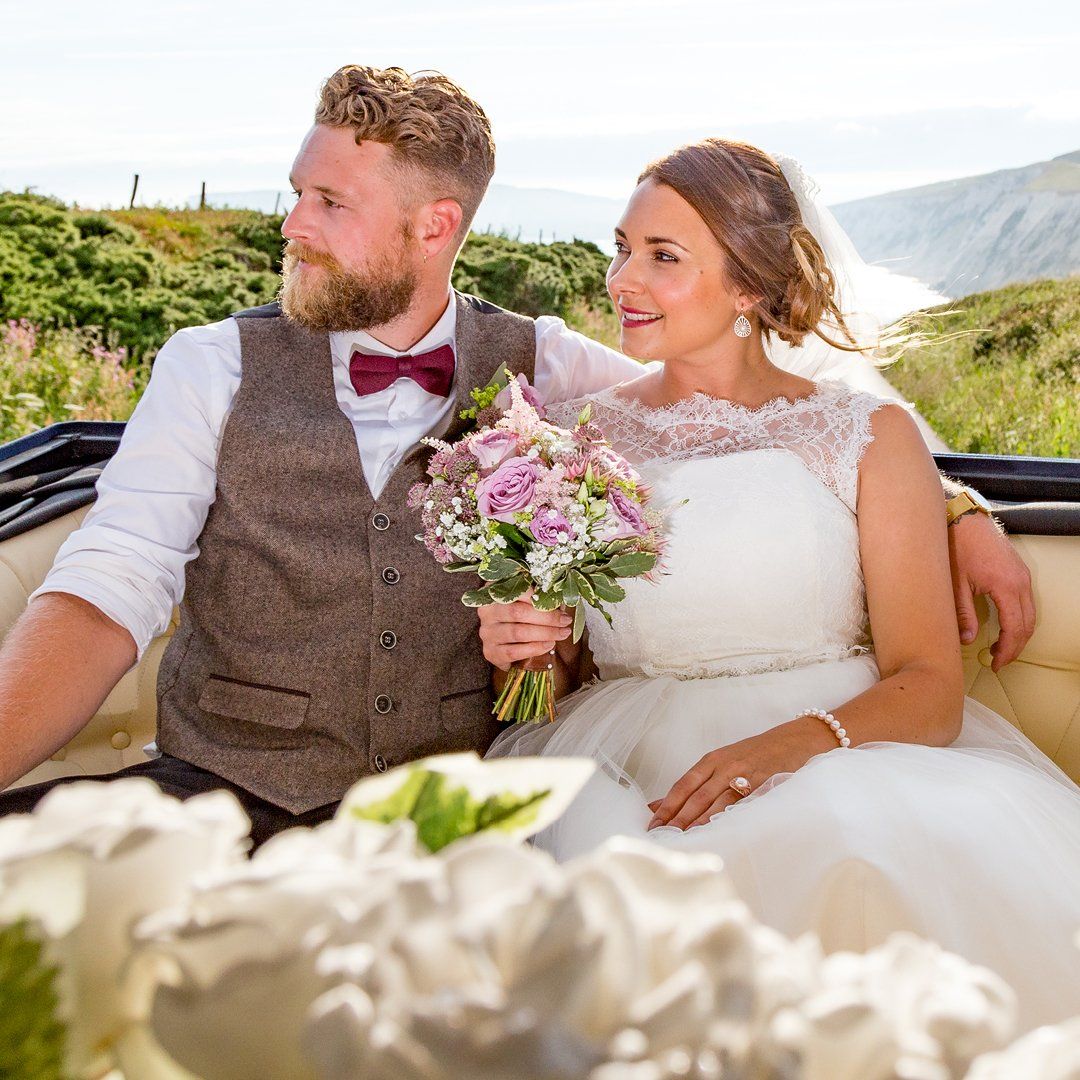 Bride and groom in a wedding carriage with flowers, looking out at a scenic landscape.