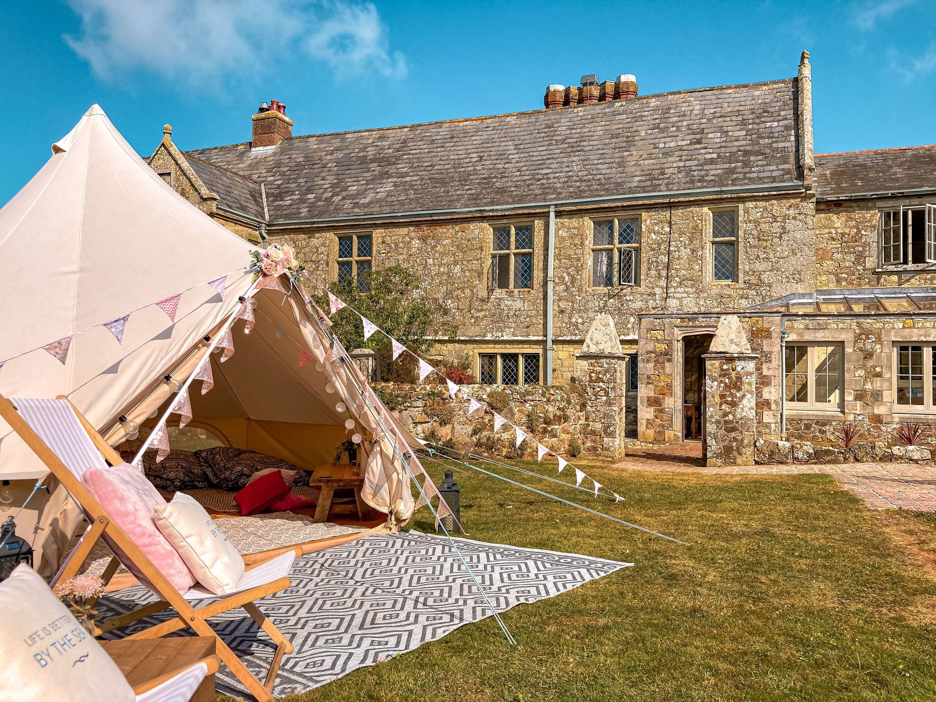 A canvas tent with chairs and bunting in front of a stone building with windows.