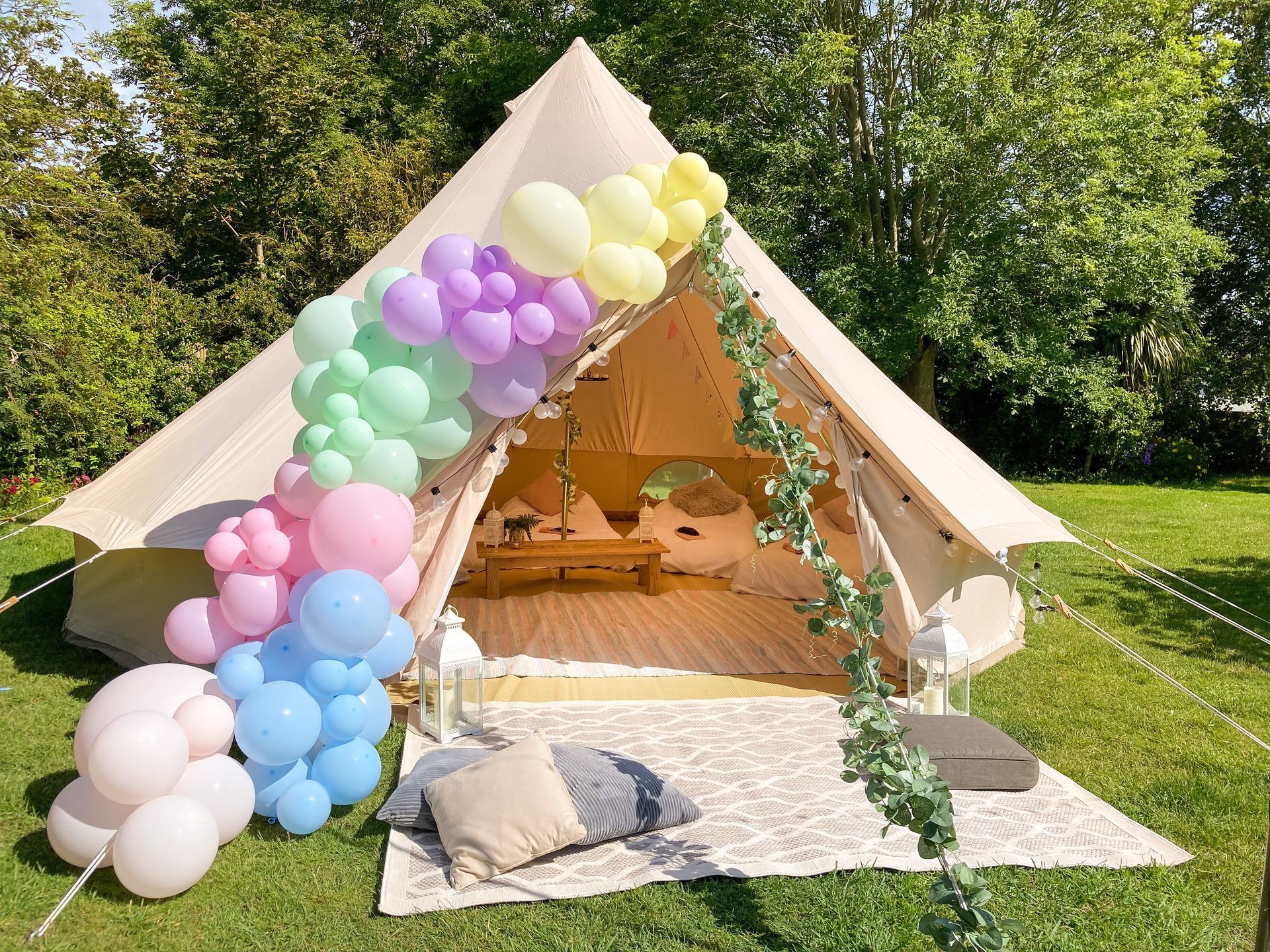 A decorated canvas tent in a garden, adorned with pastel balloons and greenery.