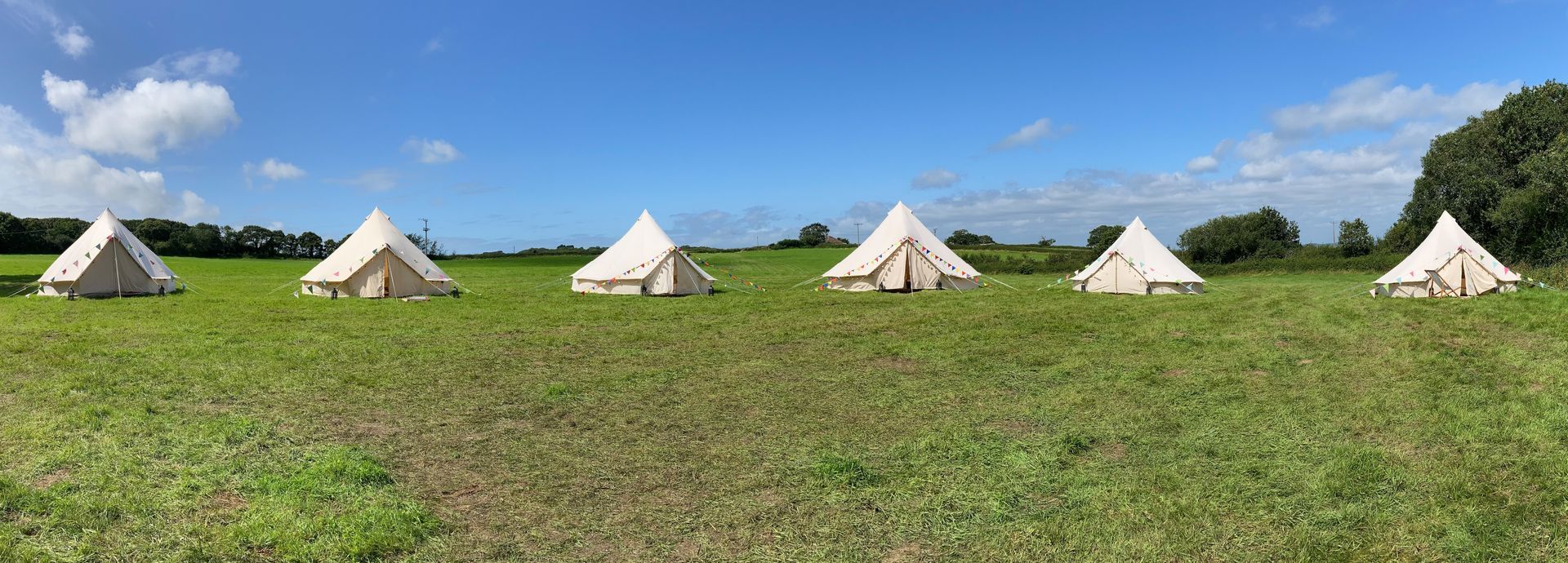 Six bell tents on green grass under a clear blue sky.