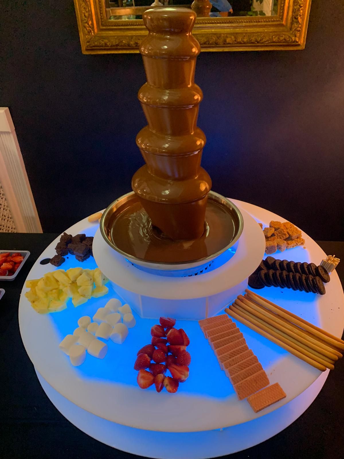 Chocolate fountain with various dipping items on a tiered, lit-up display.