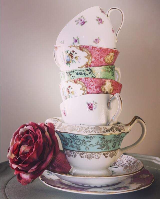 Stacked floral teacups, teal and pink hues, rose next to the bottom cup.