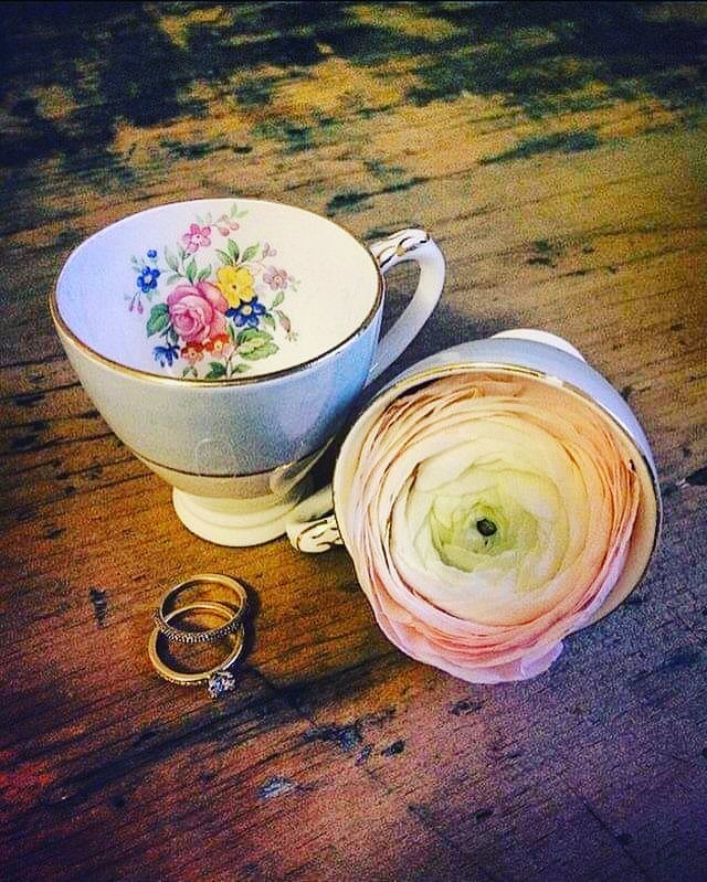 Two teacups, one holding a flower, rings on wood. Teacup has floral pattern.