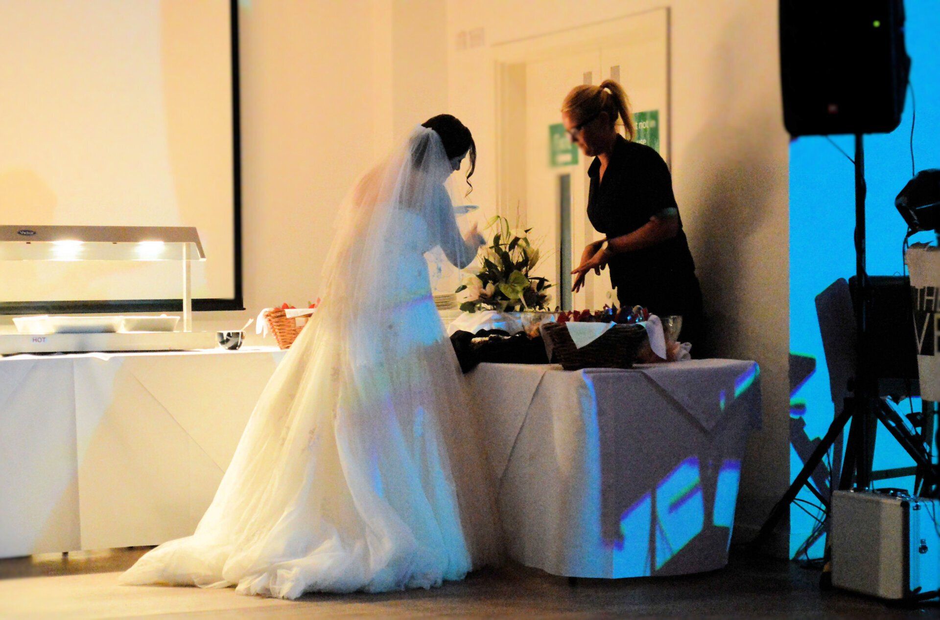 Bride and caterer at wedding buffet table, with flowers, food, and projection on the tablecloth.