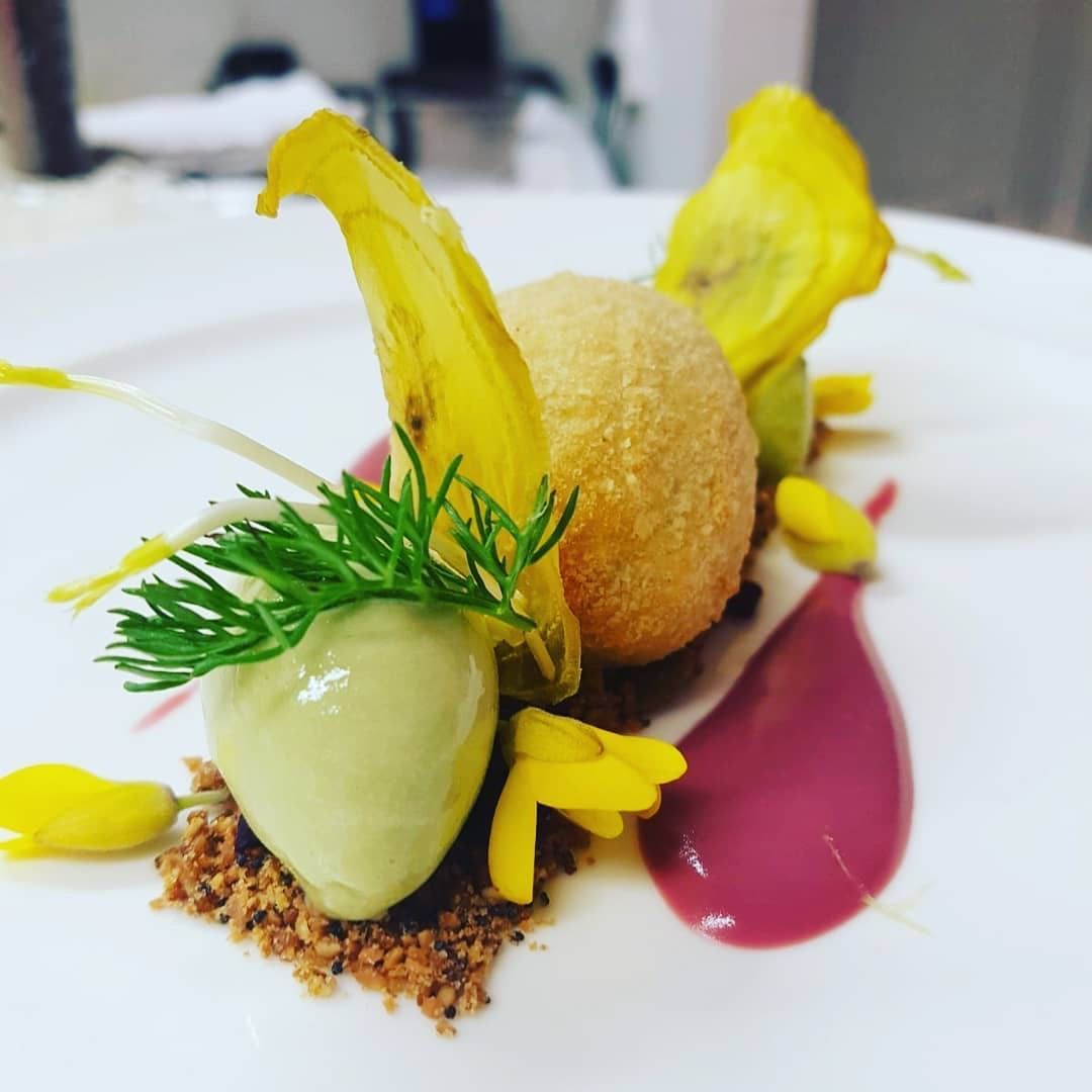 Gourmet plate with a fried ball, green puree, yellow flowers, and red sauce on a white plate.