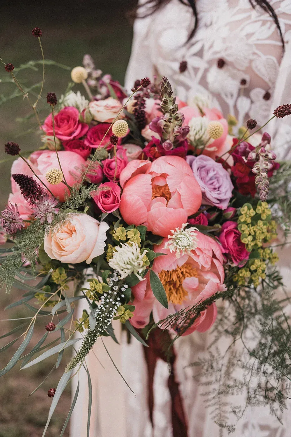 Woman holding a vibrant bouquet of pink and peach peonies, roses, and greenery.