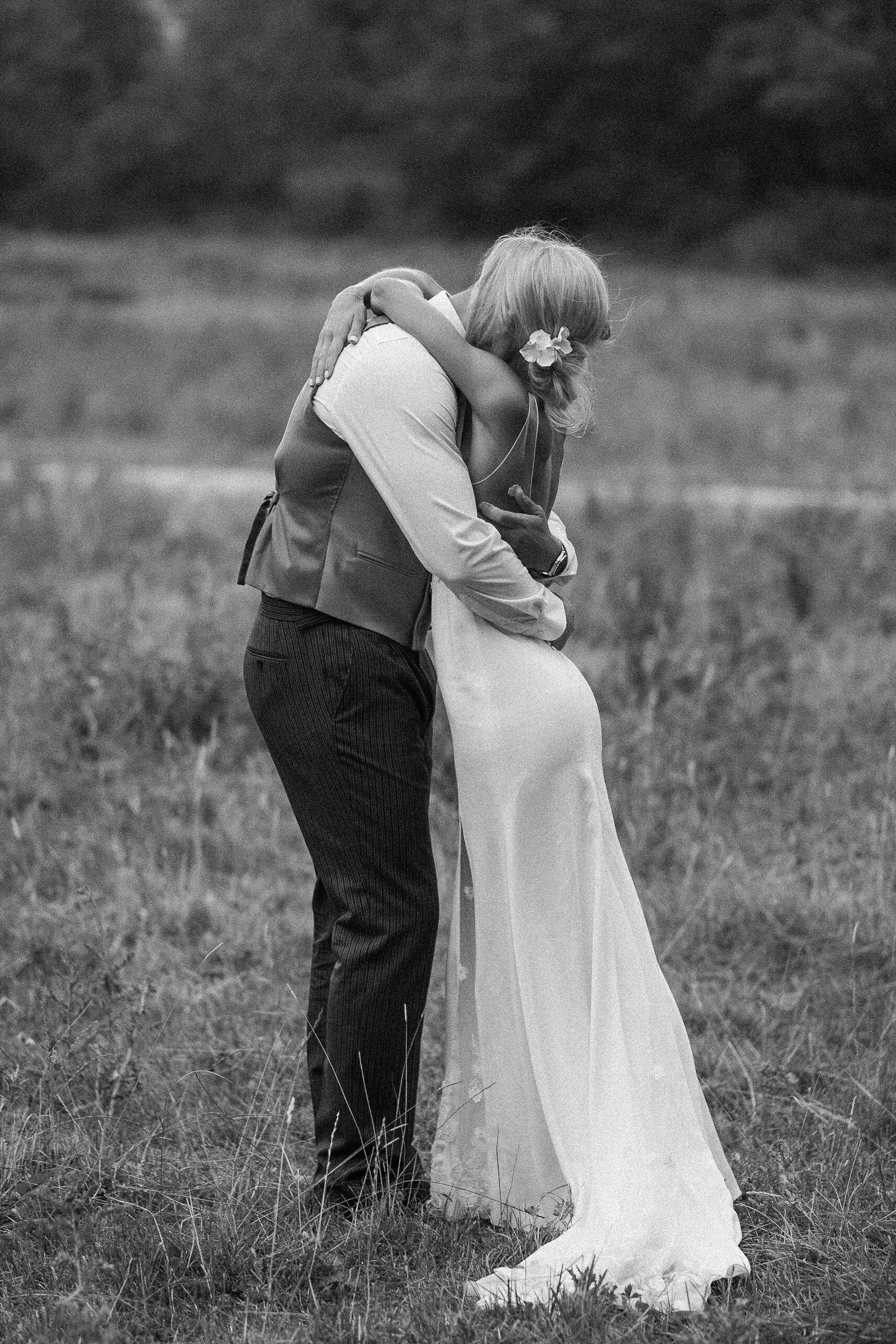 Couple embracing outdoors; the woman in a wedding dress, the man in a vest.