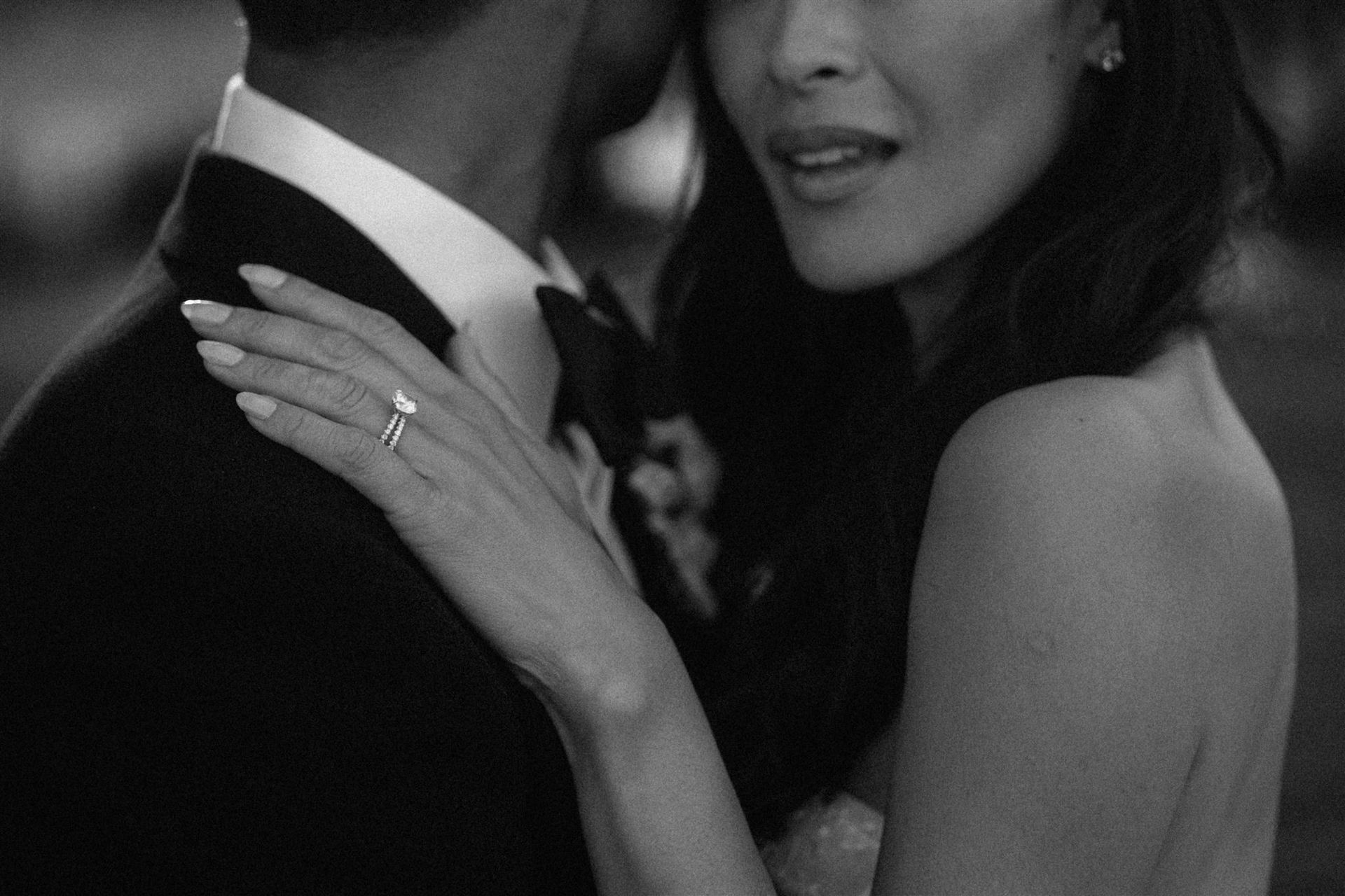Woman in strapless dress, arm around man in suit; diamond engagement ring.