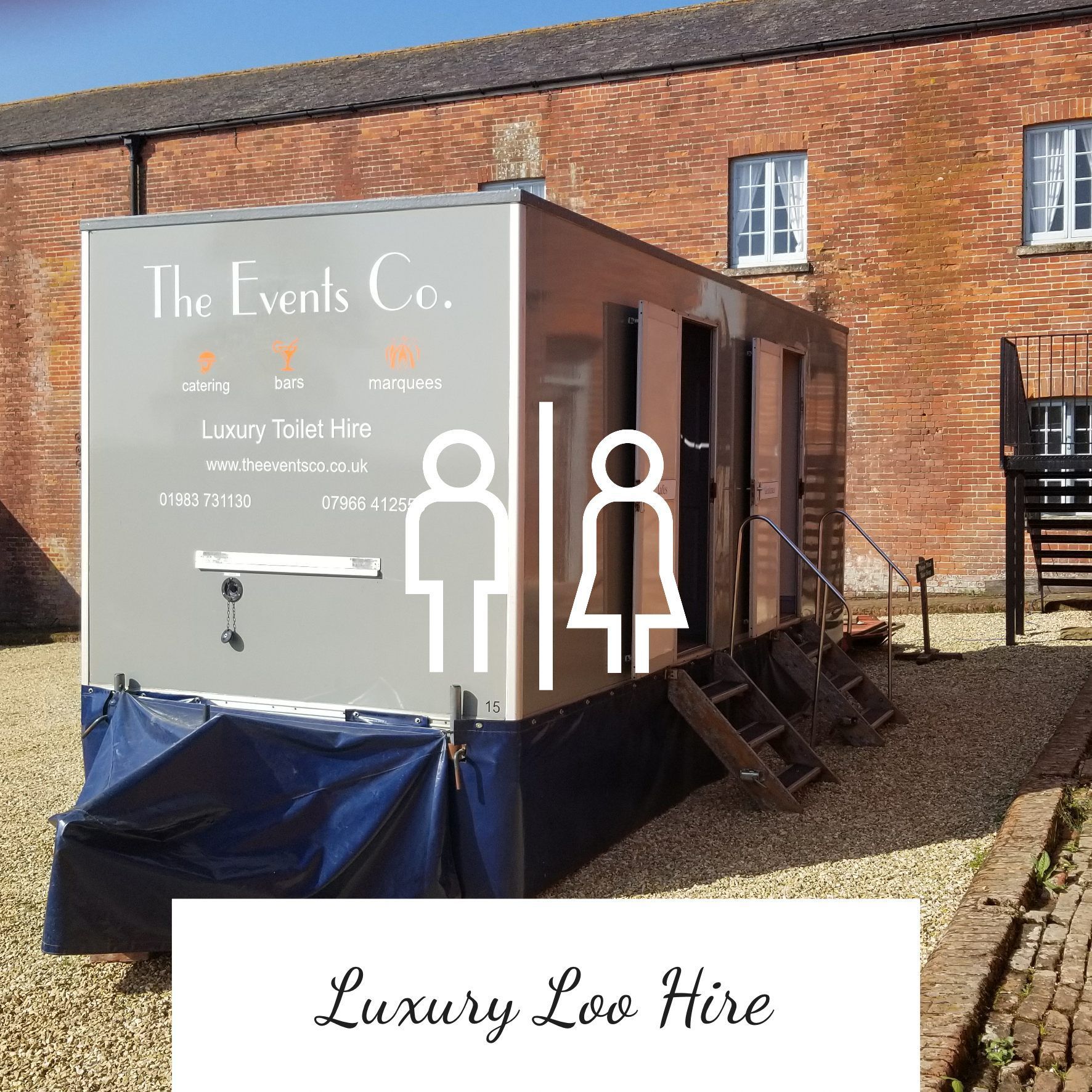 Luxury restroom trailer for hire, gray with white text and gender symbols; set on gravel.
