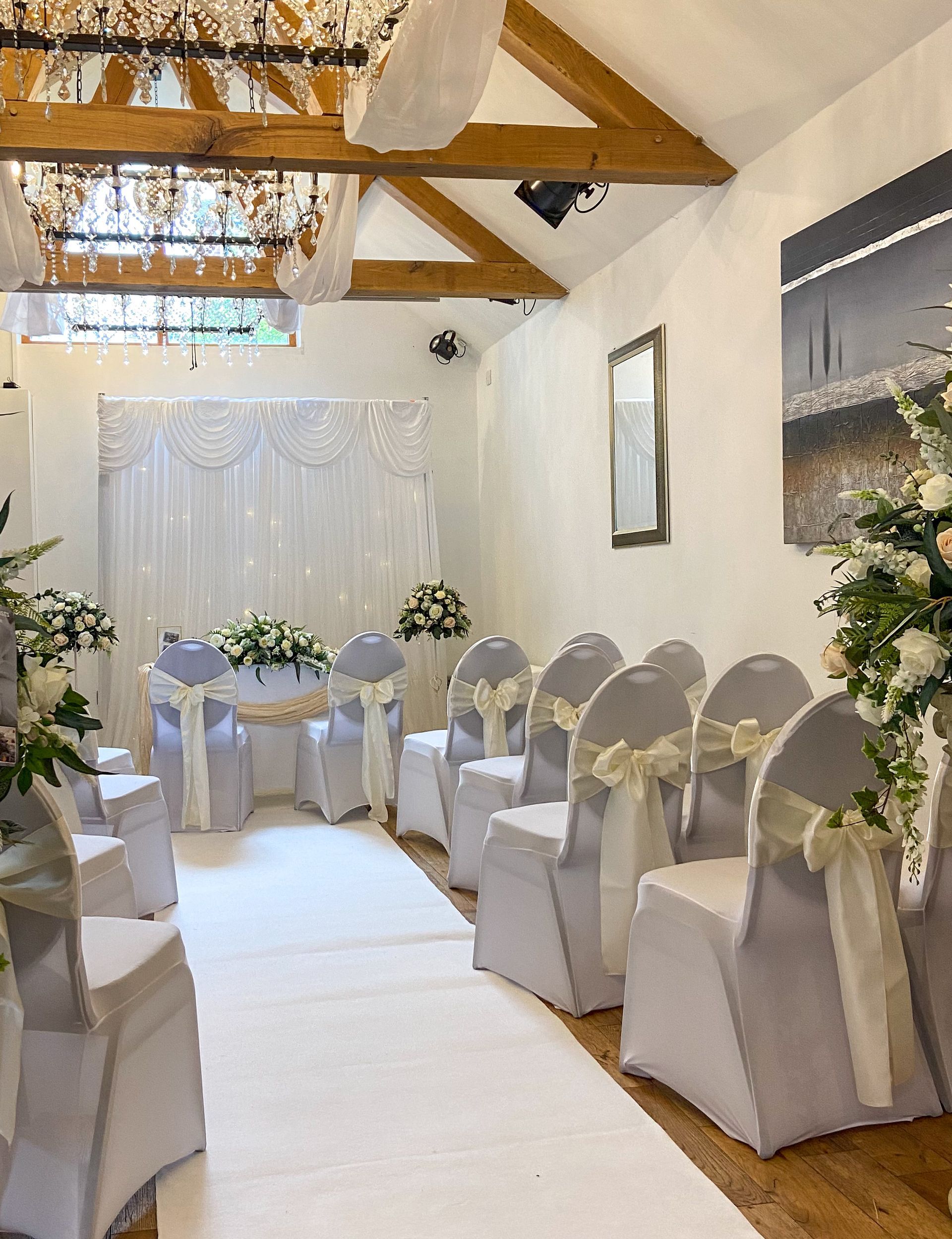 Wedding ceremony venue with white chairs, aisle, and floral arrangements.