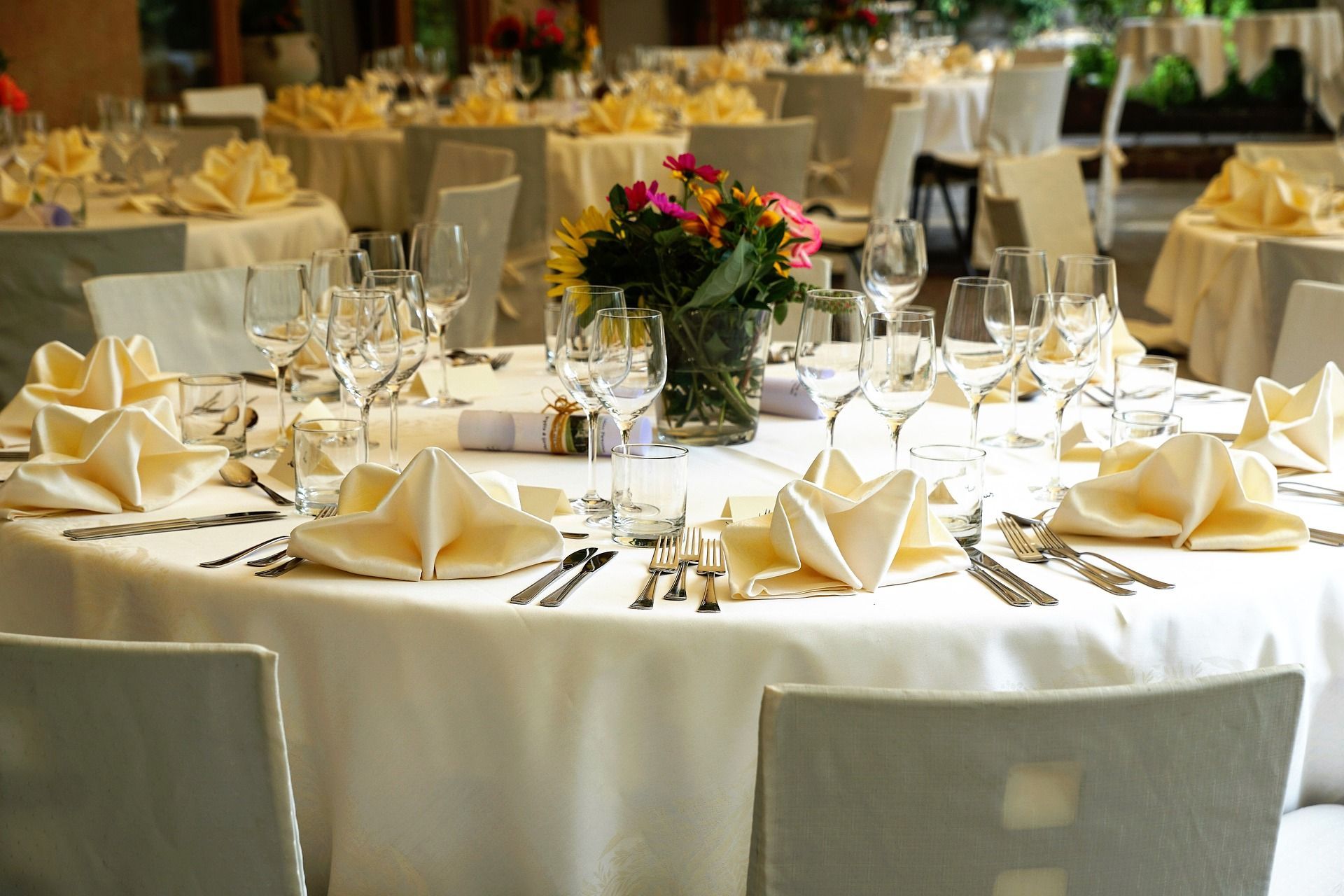 Round tables set for a banquet with white linens, cream napkins, silverware, glasses, and a floral centerpiece.