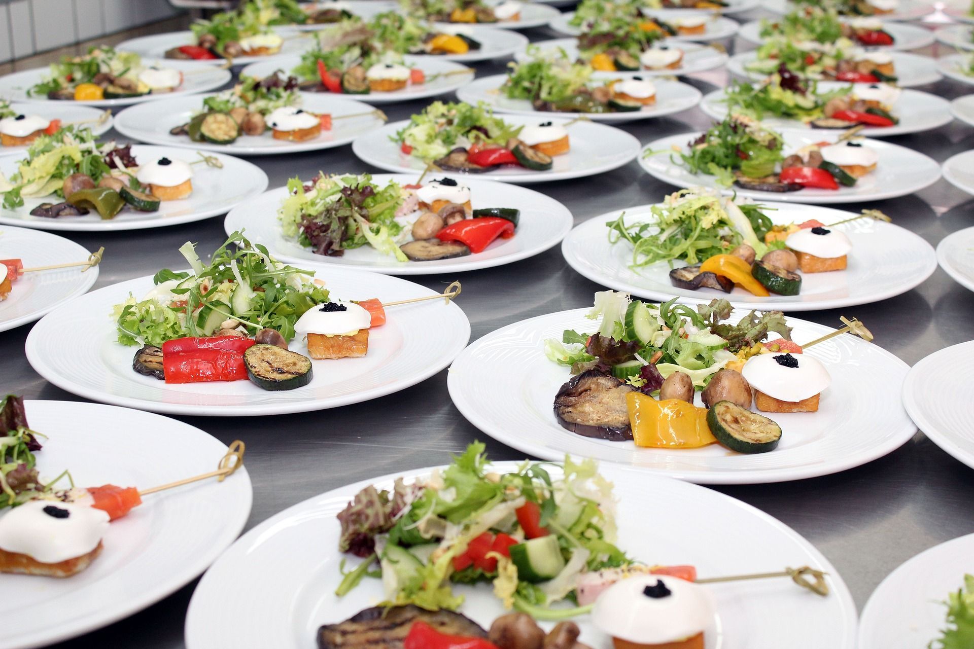 Plates of prepared food on a table, including salad, grilled vegetables, and appetizers, ready to serve.