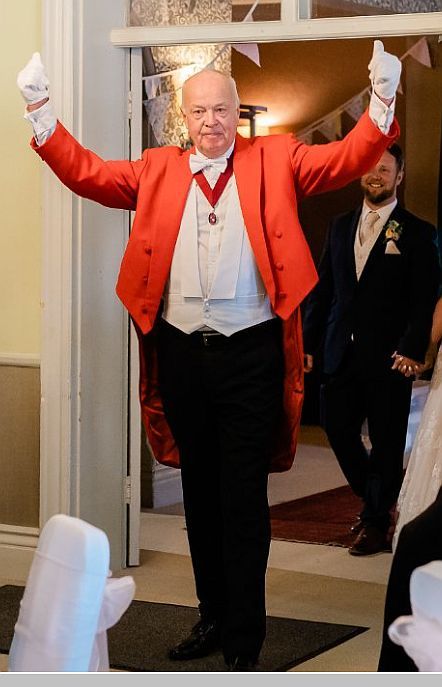 Beefeater in red coat with arms raised, wearing gloves, in doorway at event.