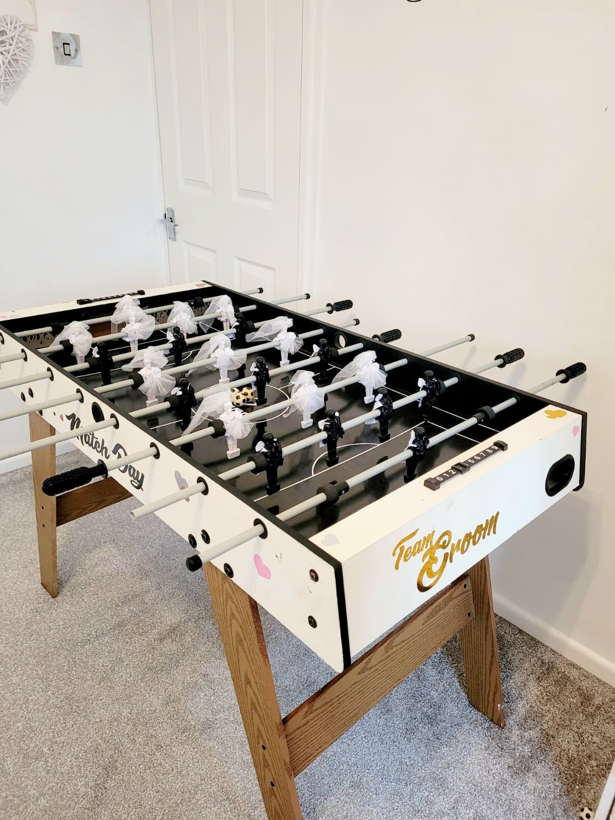 Foosball table with white and black players, on a wooden stand, in a room.