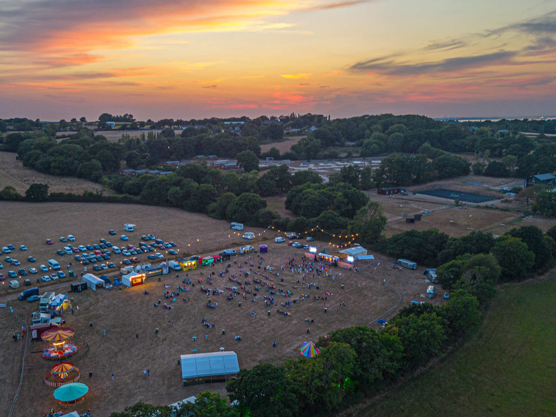 Aerial view of an outdoor event at sunset with a crowd, food stalls, and a fairground ride.