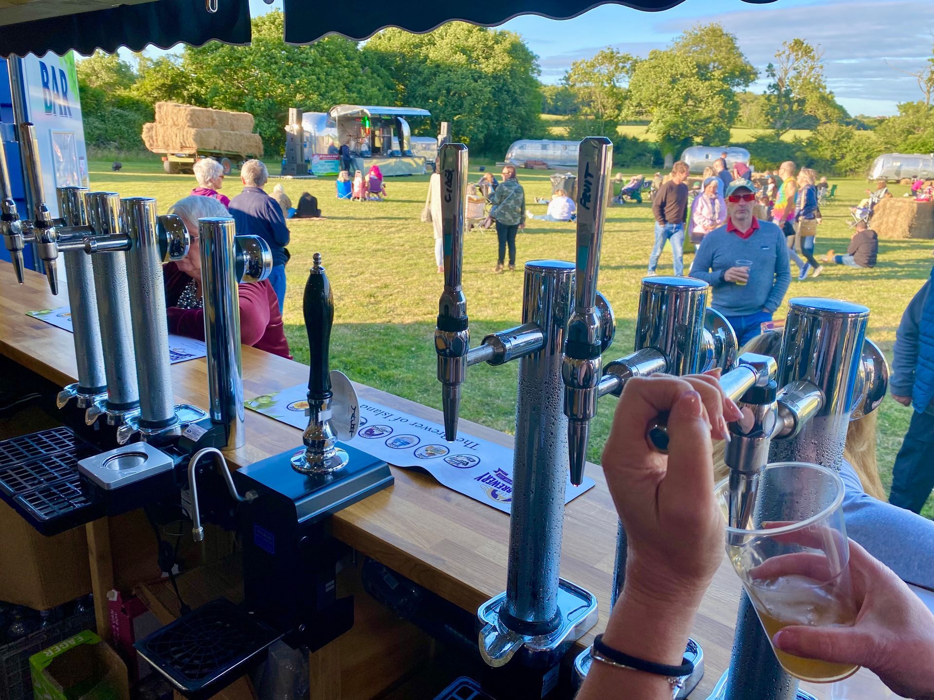 Bar with taps pouring beer at an outdoor event, people in the background.