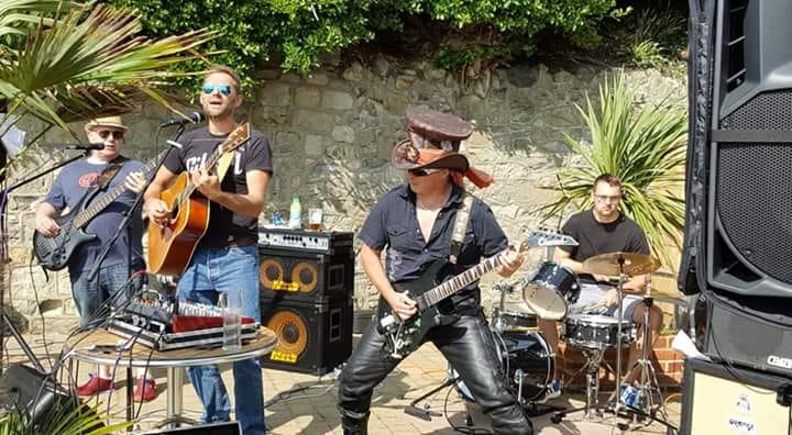 Band playing outdoors: a guitarist with a pirate hat performs with bandmates.