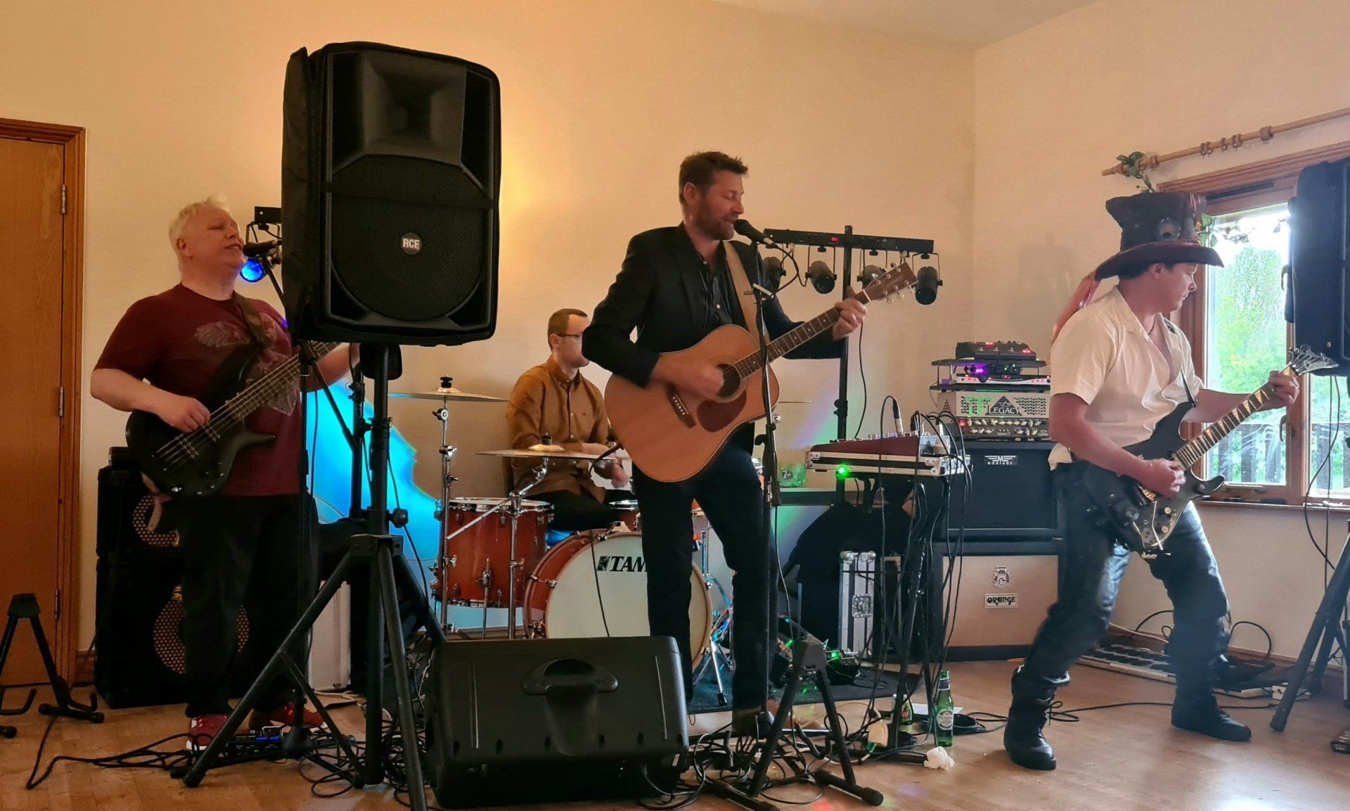 Band playing live music indoors: guitarist singing, drummer, bassist, and another guitarist.