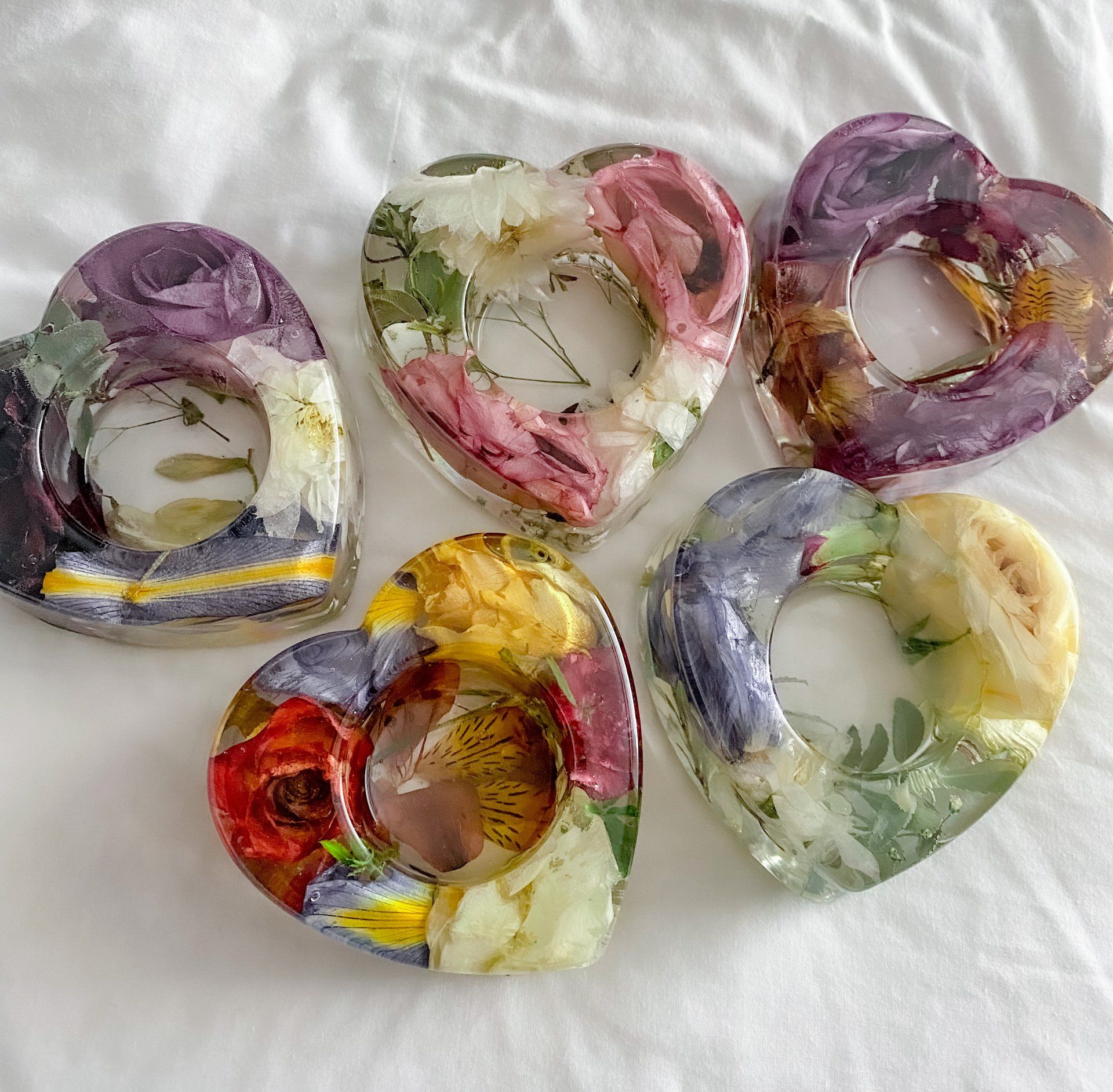 Heart-shaped candle holders made of clear resin with dried flowers embedded.