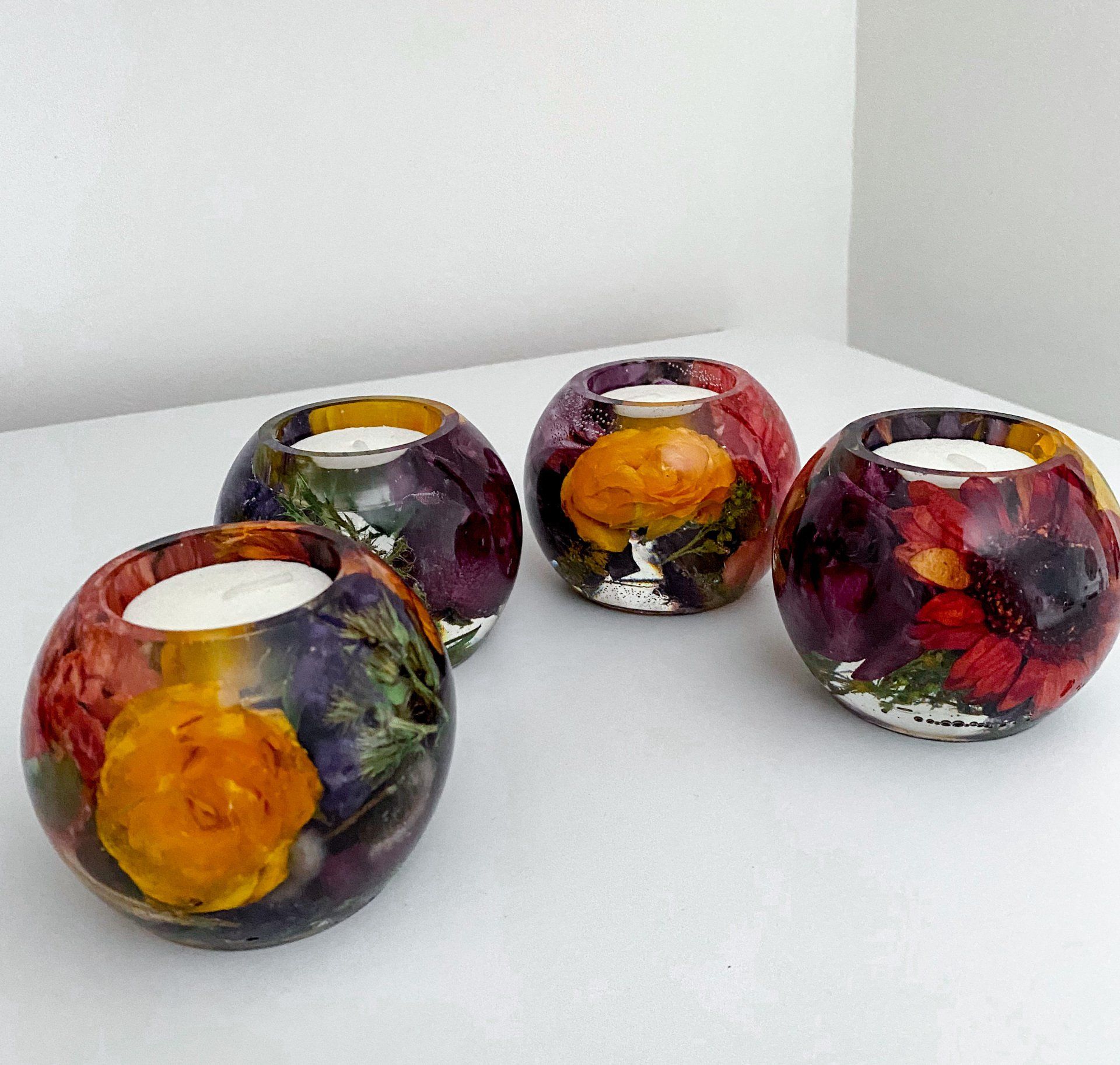 Four round candle holders with flowers encased in resin, on a white surface.