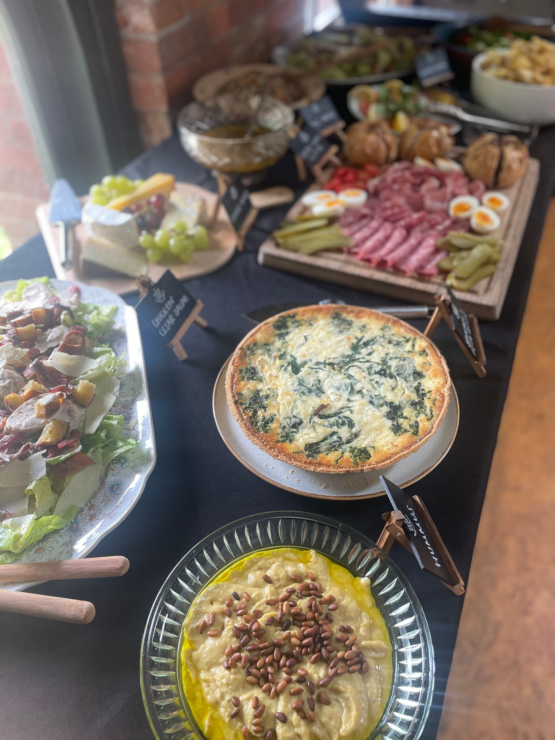 Buffet table with quiche, salad, charcuterie, cheeses, and dips.