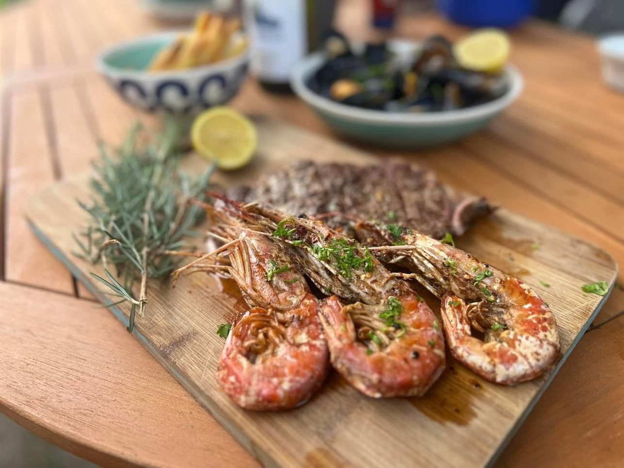 Grilled shrimp, steak, mussels, and lemon on a wooden board, outdoors on a wooden table.