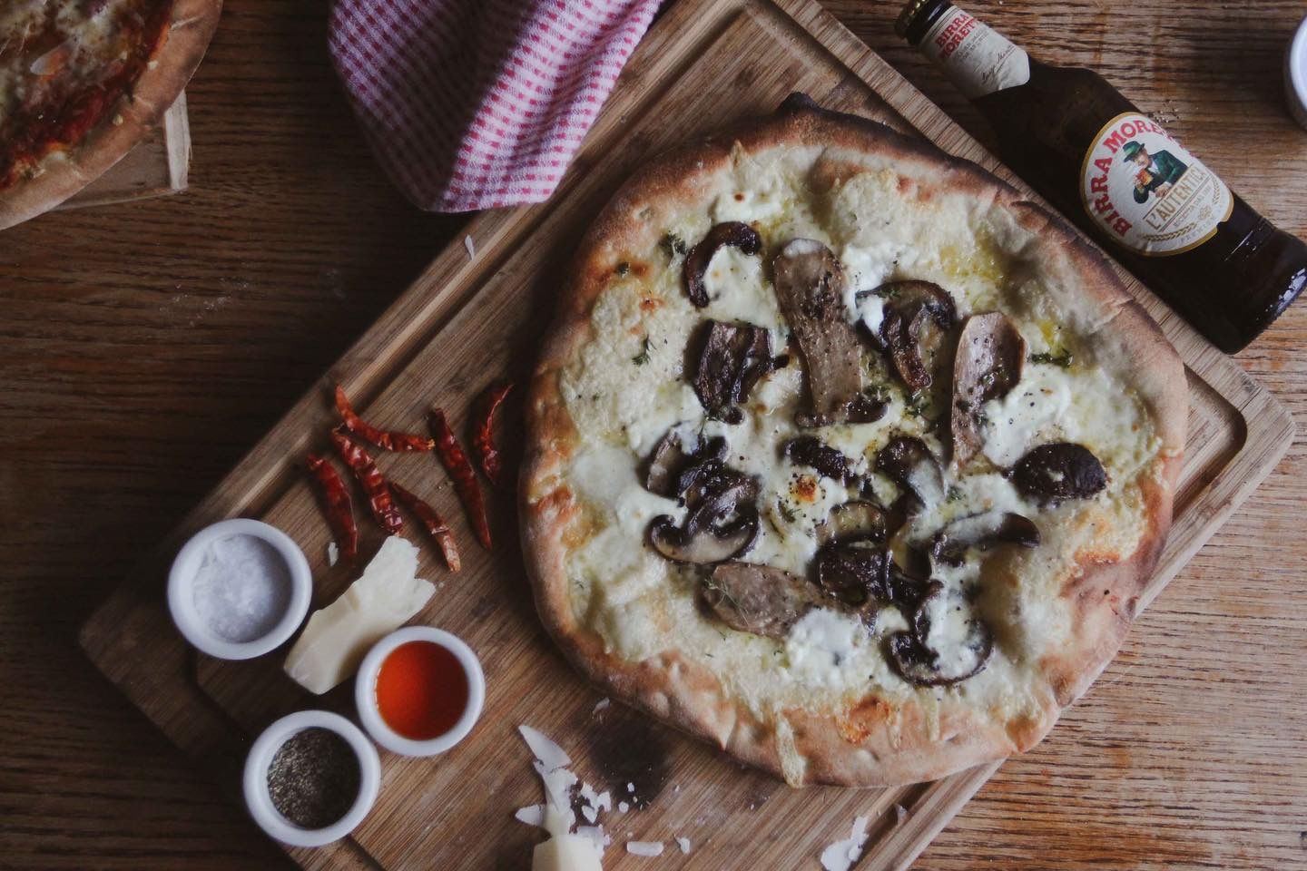 White pizza with mushrooms on a wooden board, with beer, spices, and a napkin.