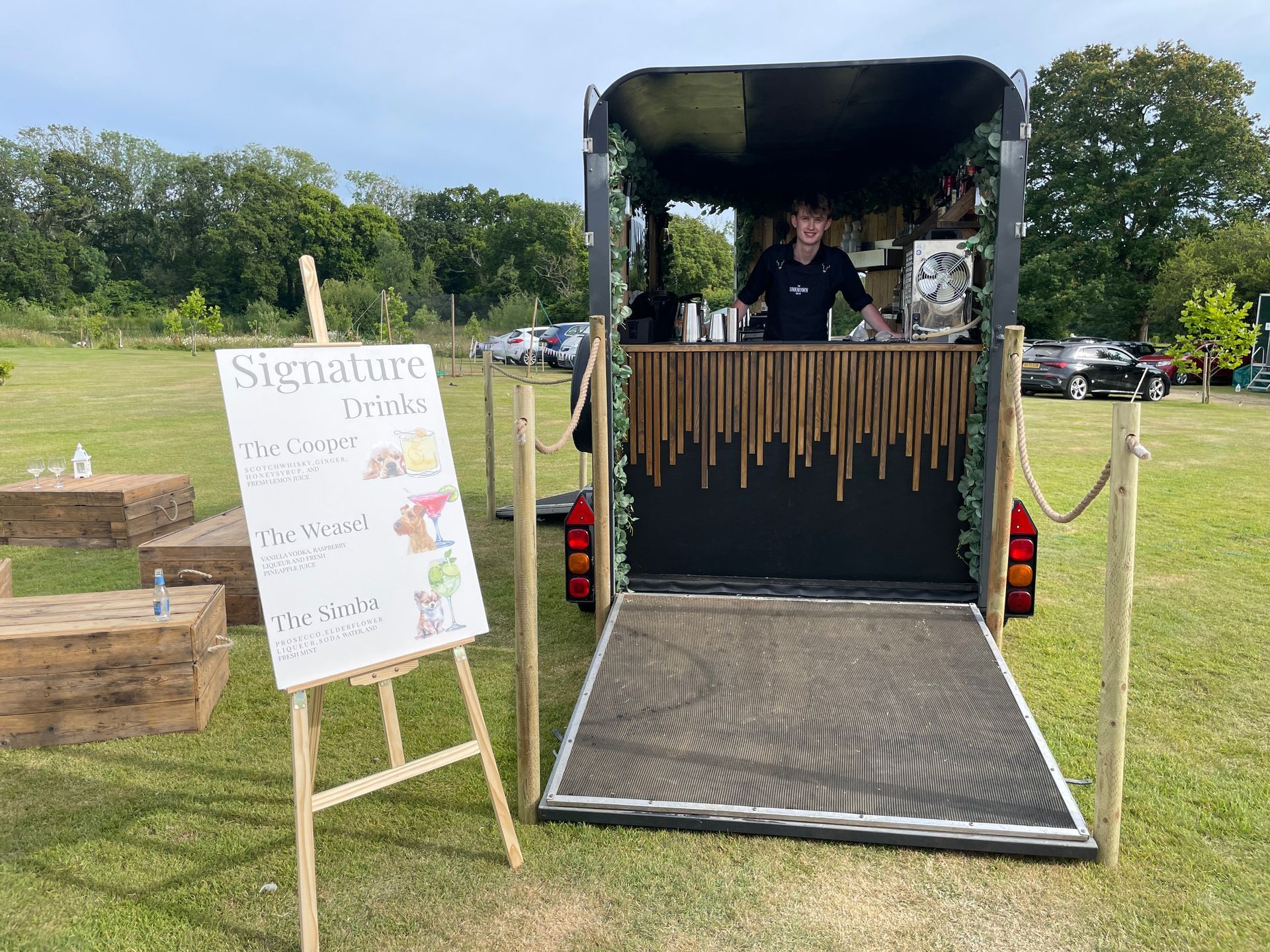 Mobile bar set up outdoors, offering signature cocktails. Bartender stands behind the bar.