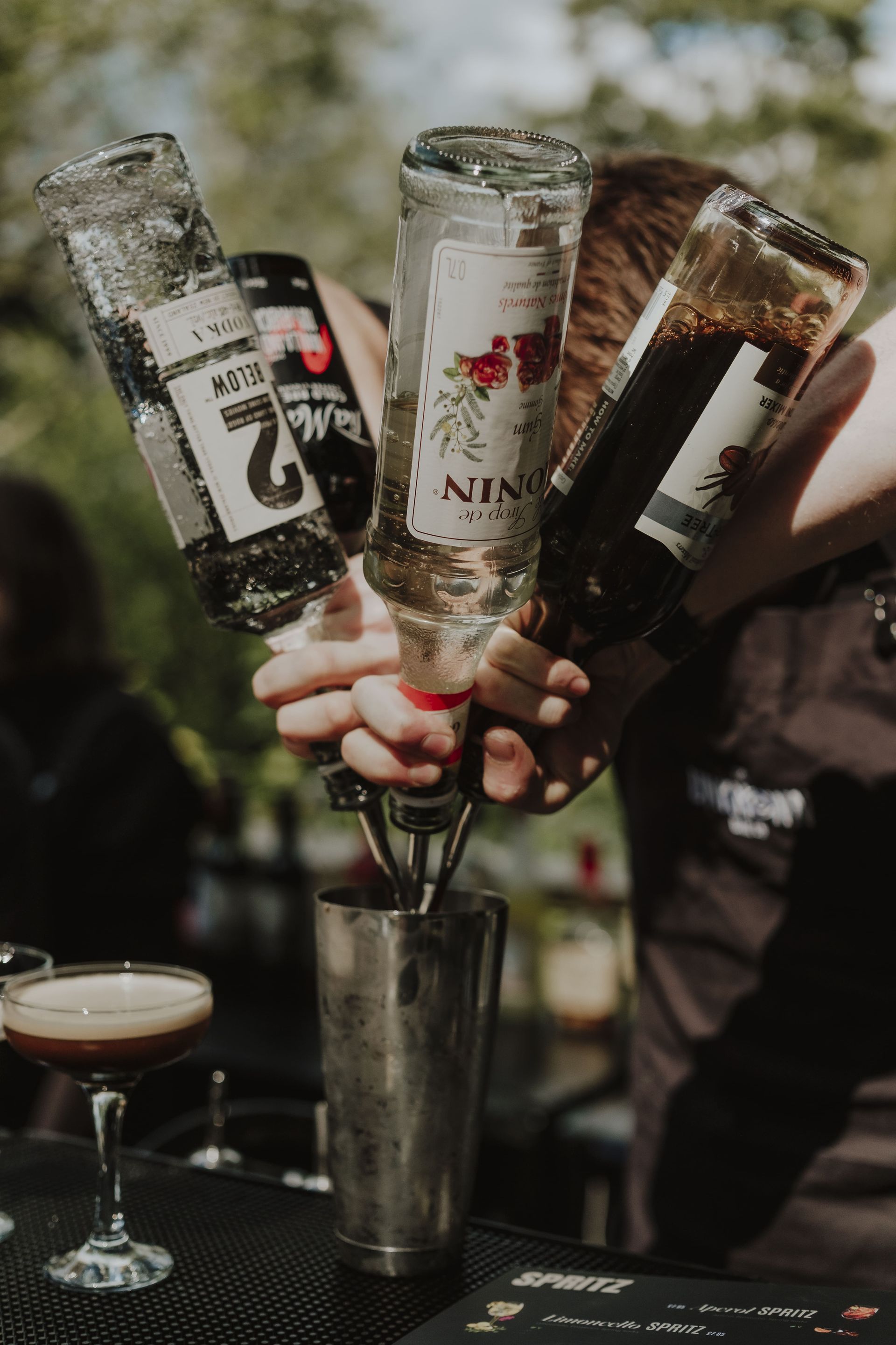 Bartender pouring liquids from bottles into a cocktail shaker, preparing a drink.